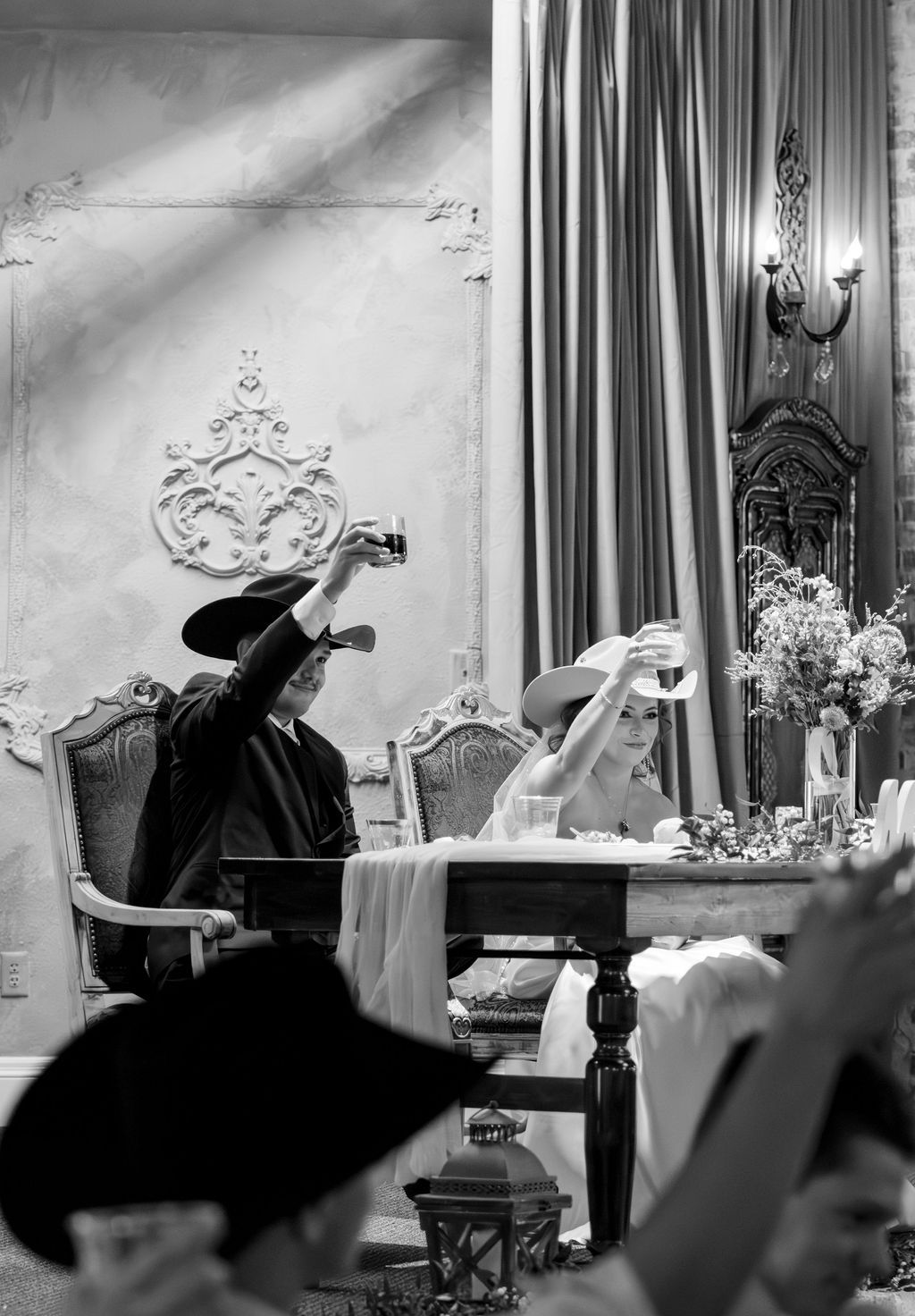 Black and white photo of a couple raising a toast at an elegant wedding reception dinner table.