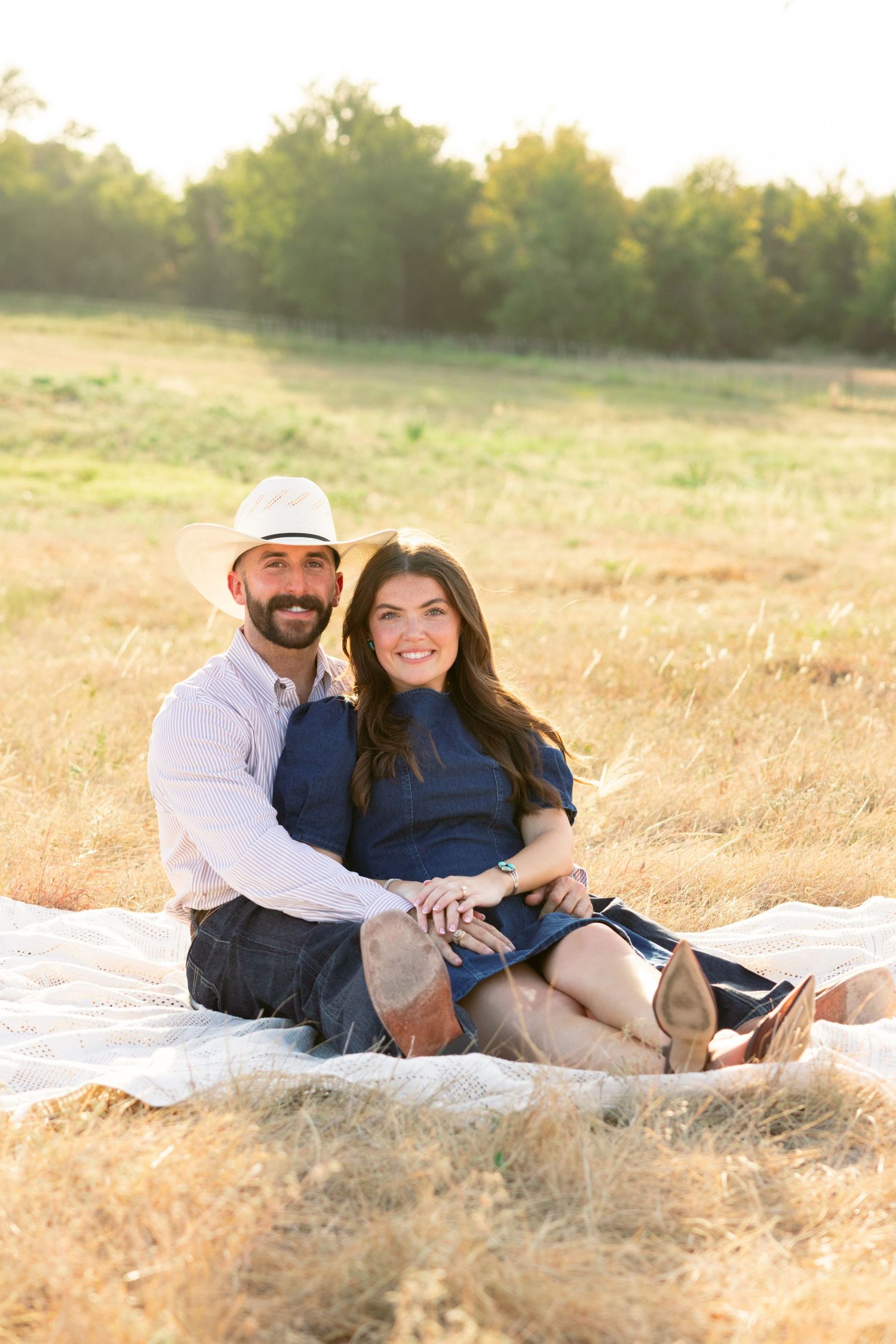 Couple sits together in golden field at sunset smiling.