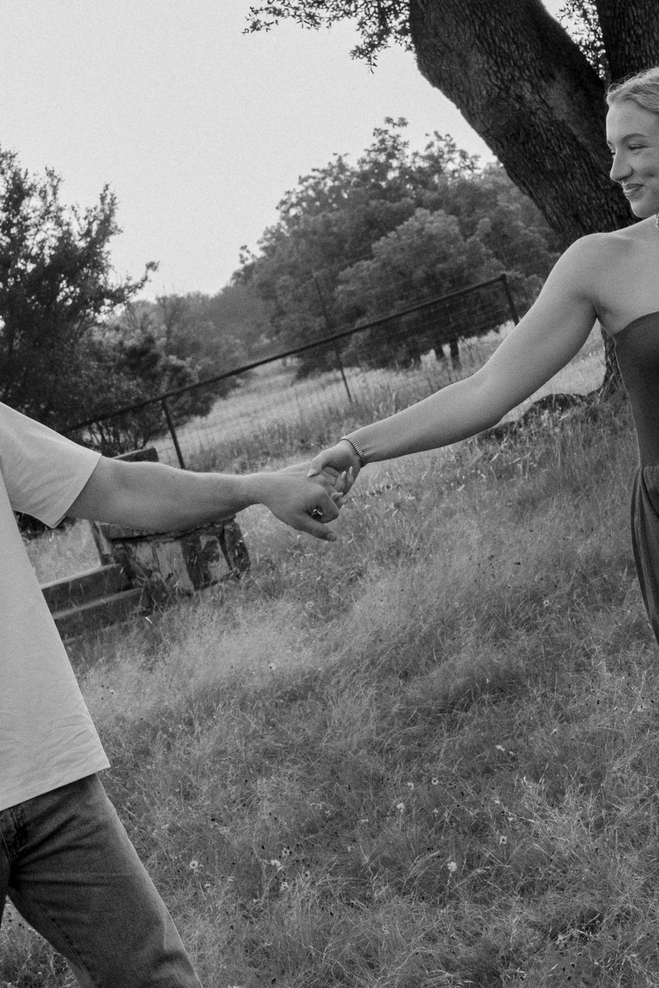 Black and white romantic photo of a couple holding hands while strolling through a lush grassy field.