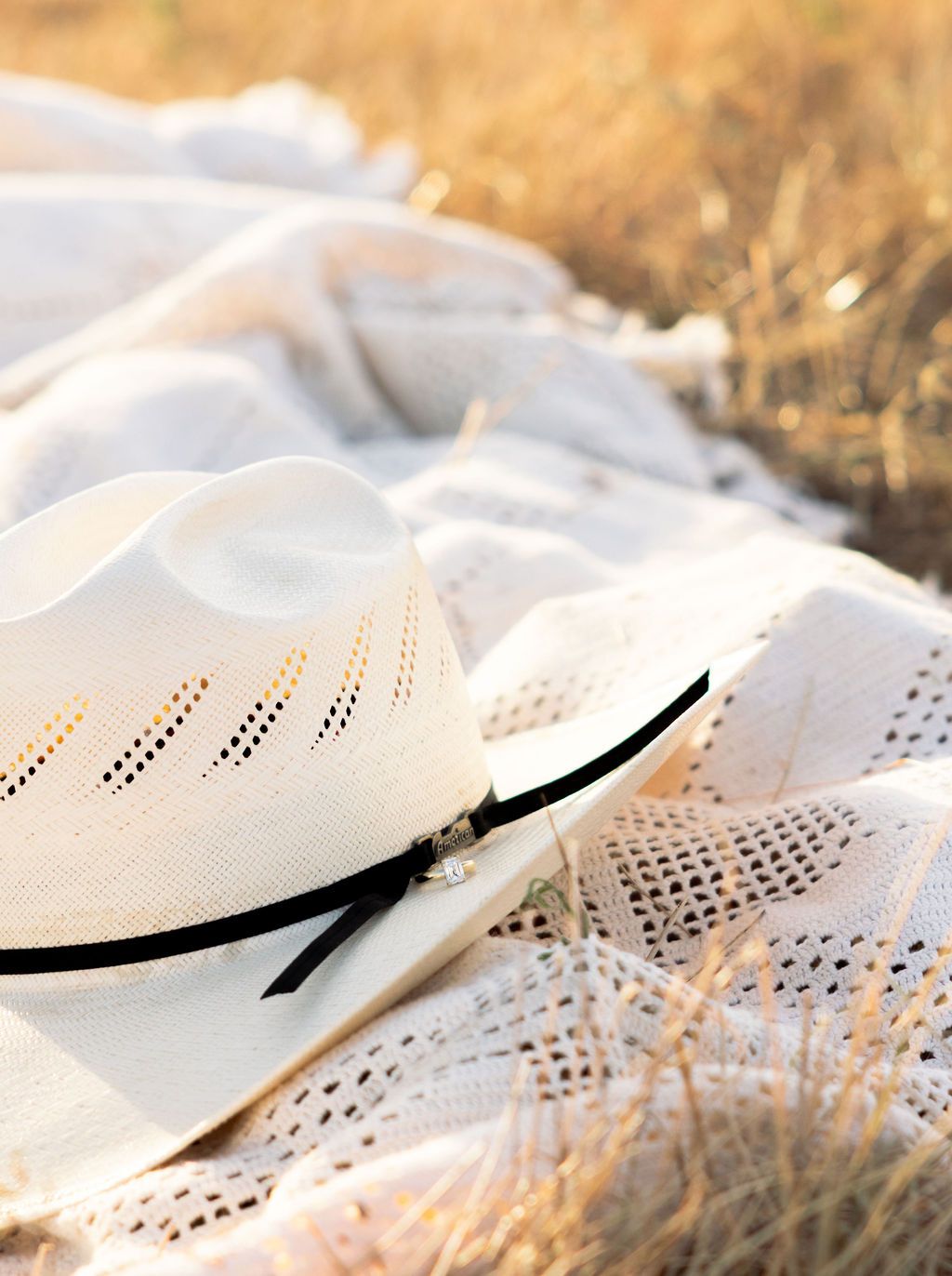 White cowboy hat with black band resting on a lace blanket in a golden grass field.