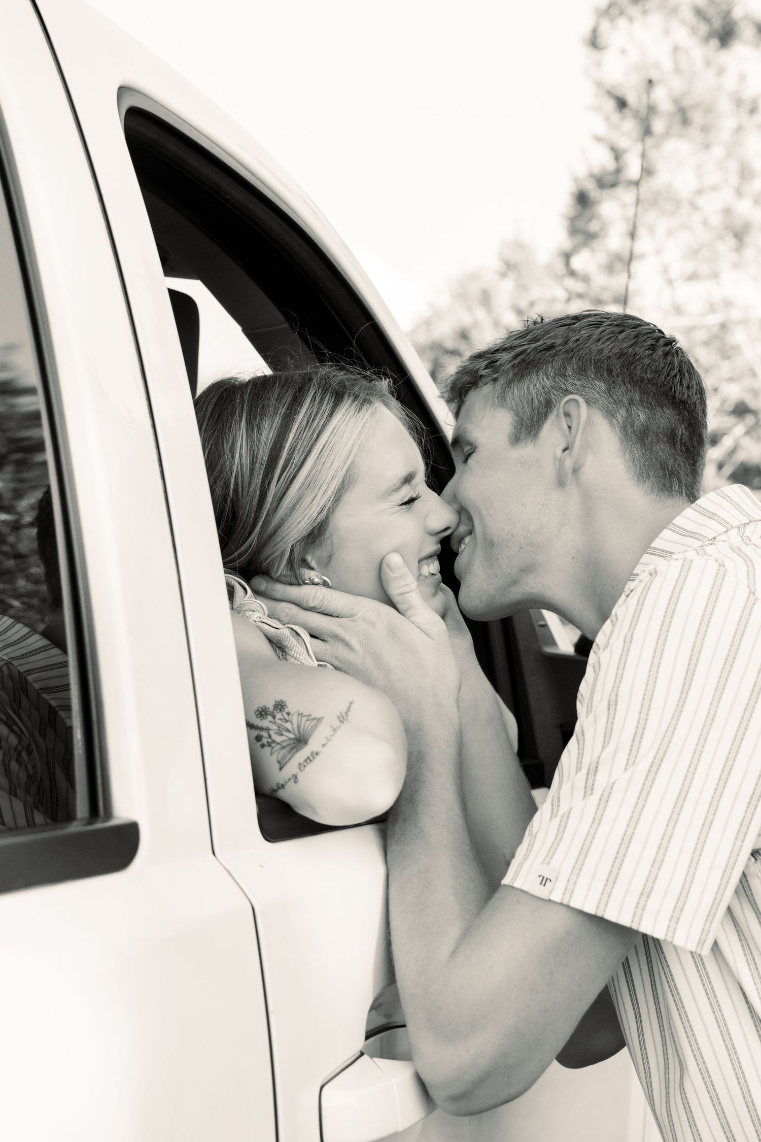 Black and white photo of a young couple sharing a romantic moment, woman leaning out of a white truck window.