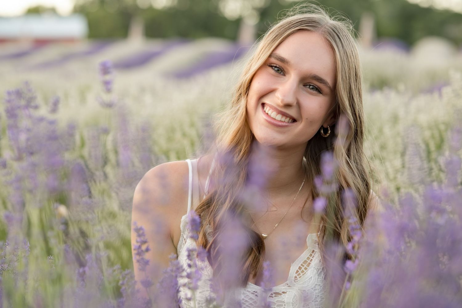 Smiling young woman with blonde hair posing in a vibrant purple lavender field on a sunny day.