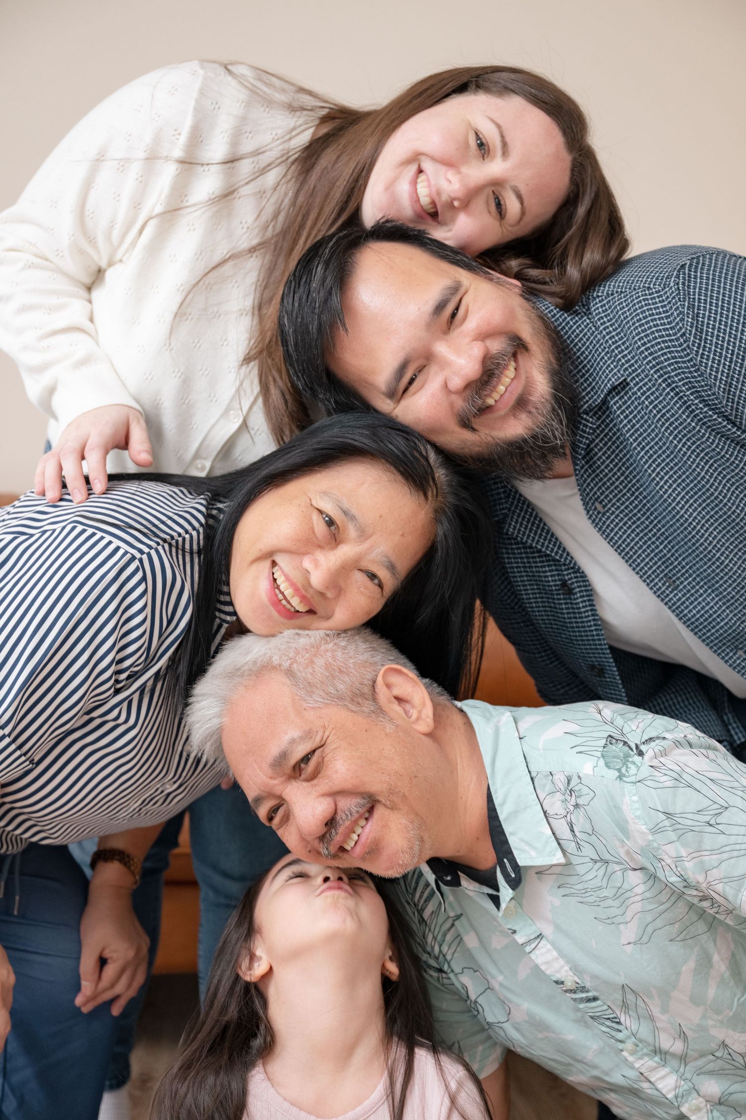 Joyful multigenerational Asian family of five huddle together smiling in a fun stacked portrait pose.