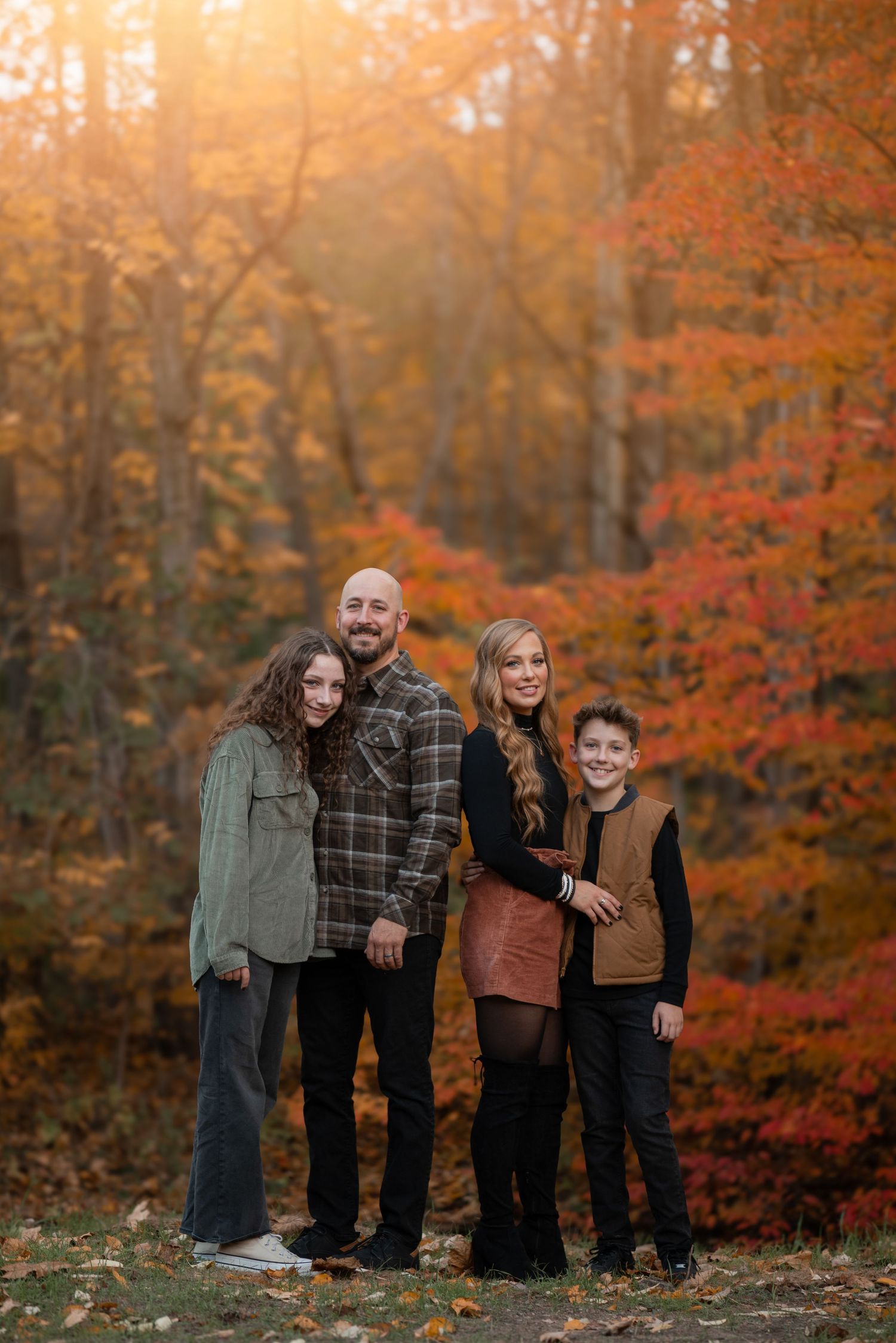 Family of four posing in autumn forest with vibrant red and orange foliage during golden hour.