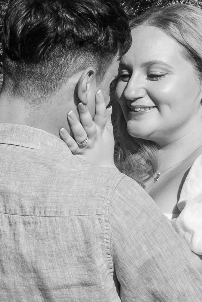 Black and white photo of a smiling woman touching a man's face in a tender romantic moment.
