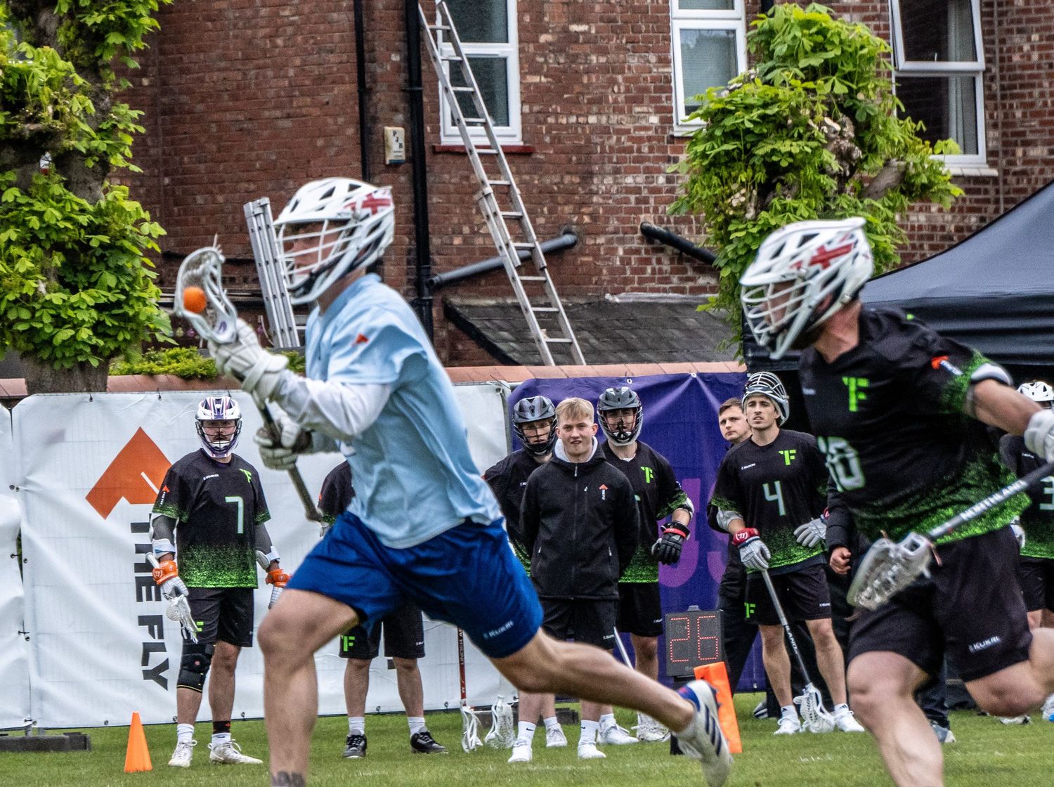 Male lacrosse players in helmets competing during an outdoor game on a green field.