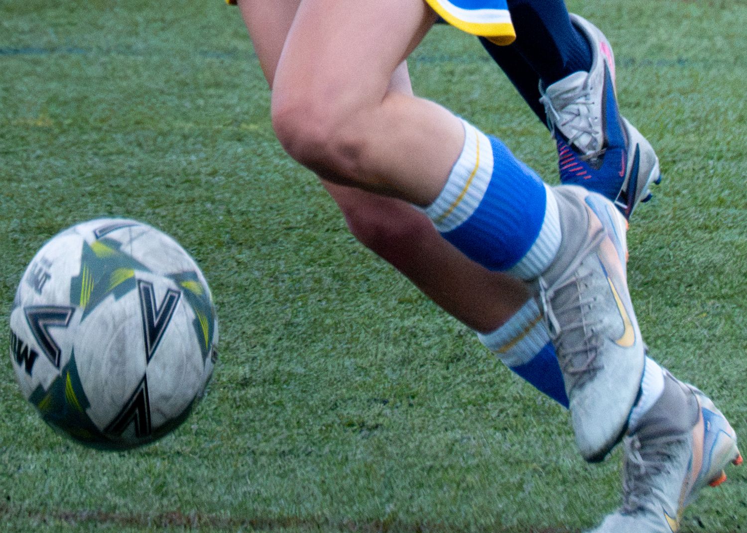 Close-up of a soccer player in blue socks and cleats dribbling a black and white football.