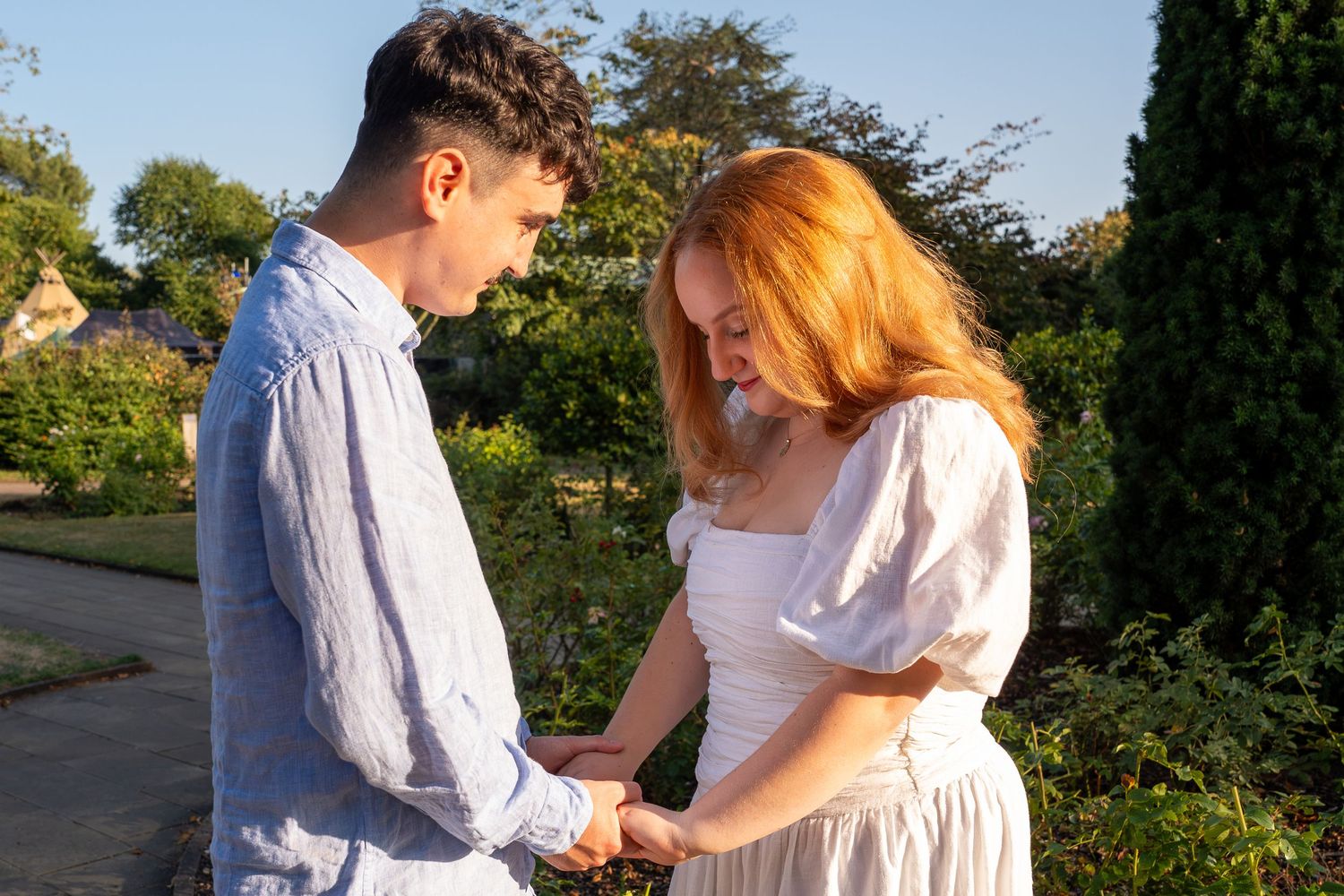 Young couple holding hands in a sunny garden, sharing a romantic moment outdoors.