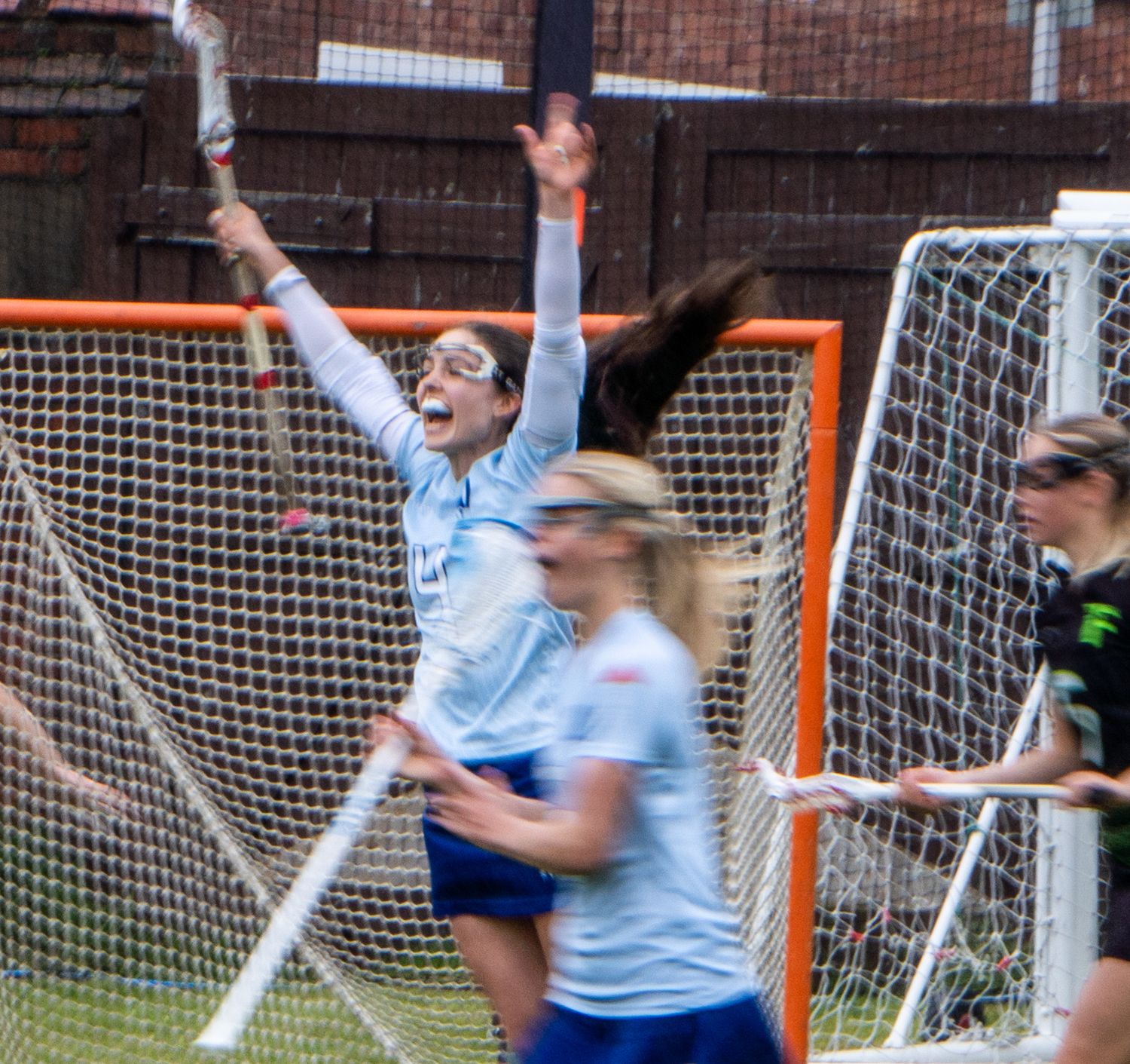 Female lacrosse player celebrates with arms raised in victory near the net.