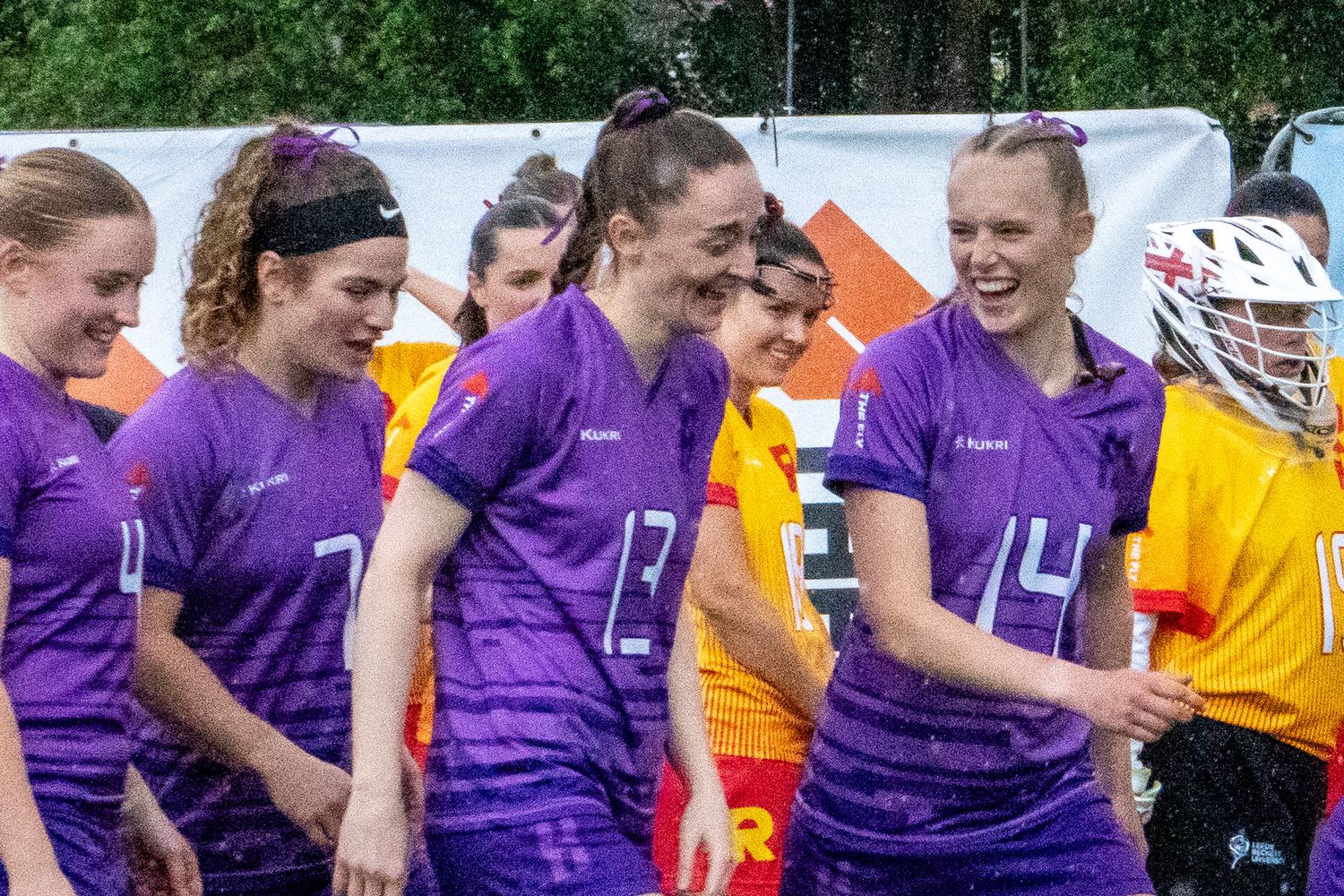 Smiling women's lacrosse team in purple uniforms walk together before a match.
