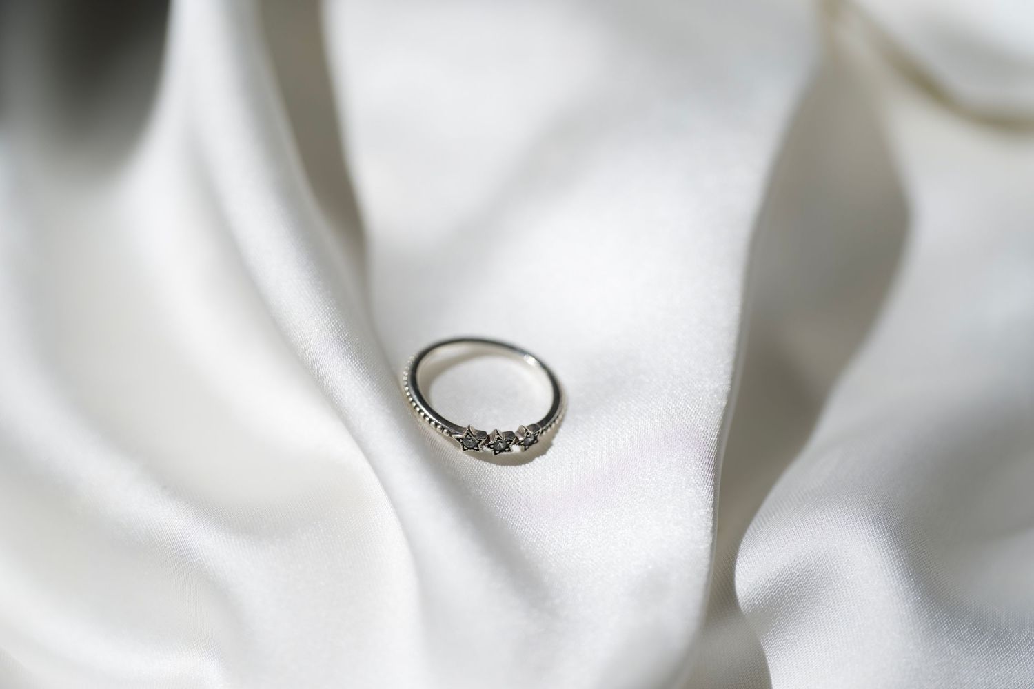 A silver diamond ring resting on white satin fabric.