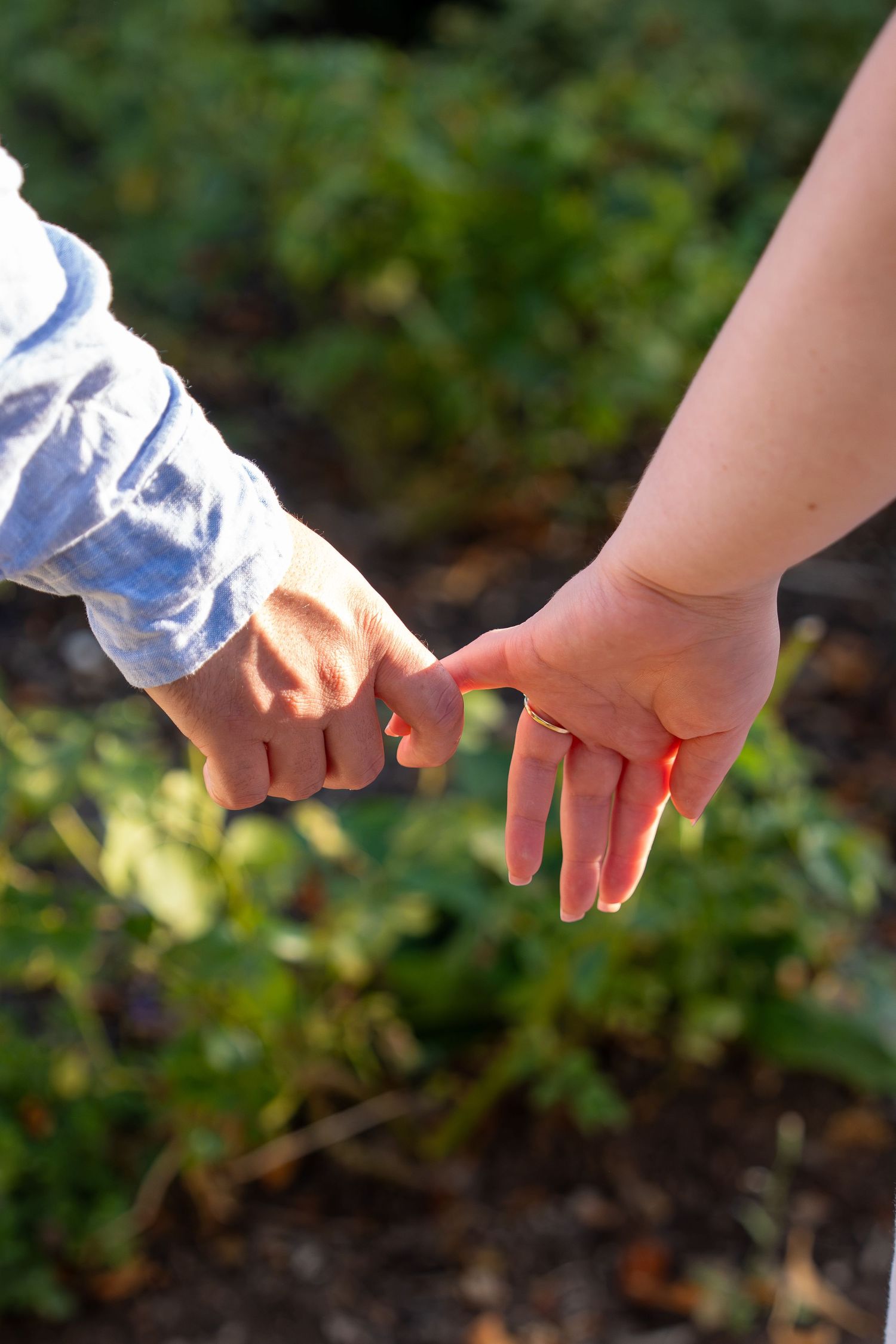 A child and adult holding pinky fingers together outdoors in a garden, symbolizing love and connection.