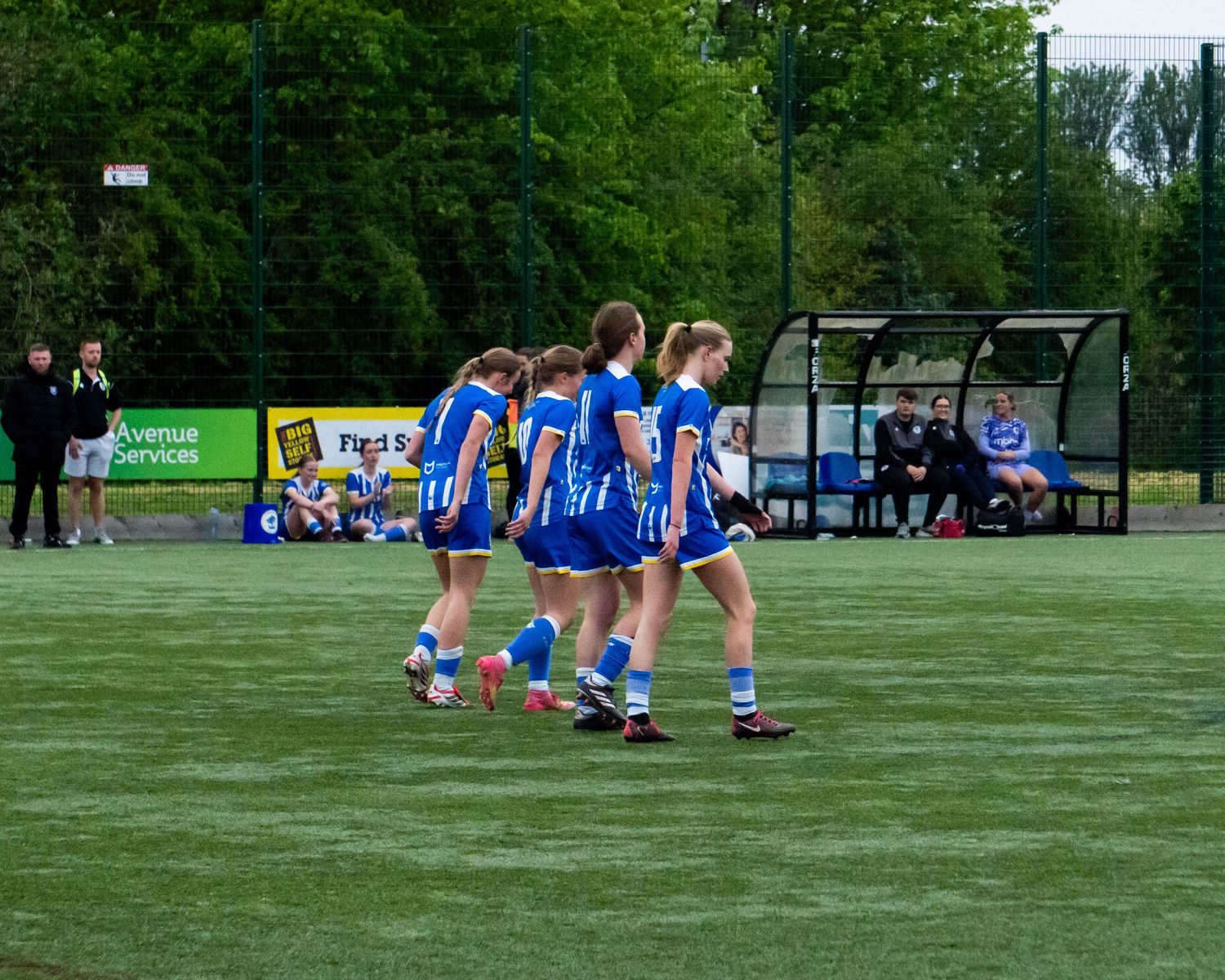 Group of female soccer players in blue and white uniforms walking together on a green turf field.