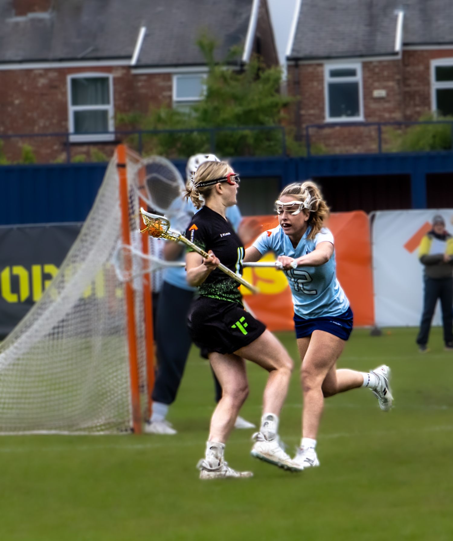 Two female lacrosse players compete for the ball during an outdoor game.