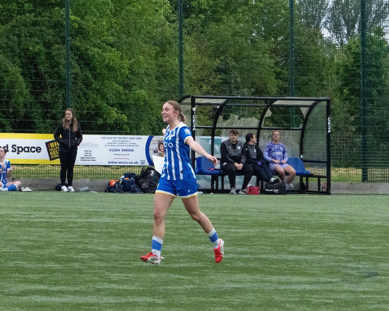 Female soccer player in blue and white kit celebrating on a green turf pitch during a match.