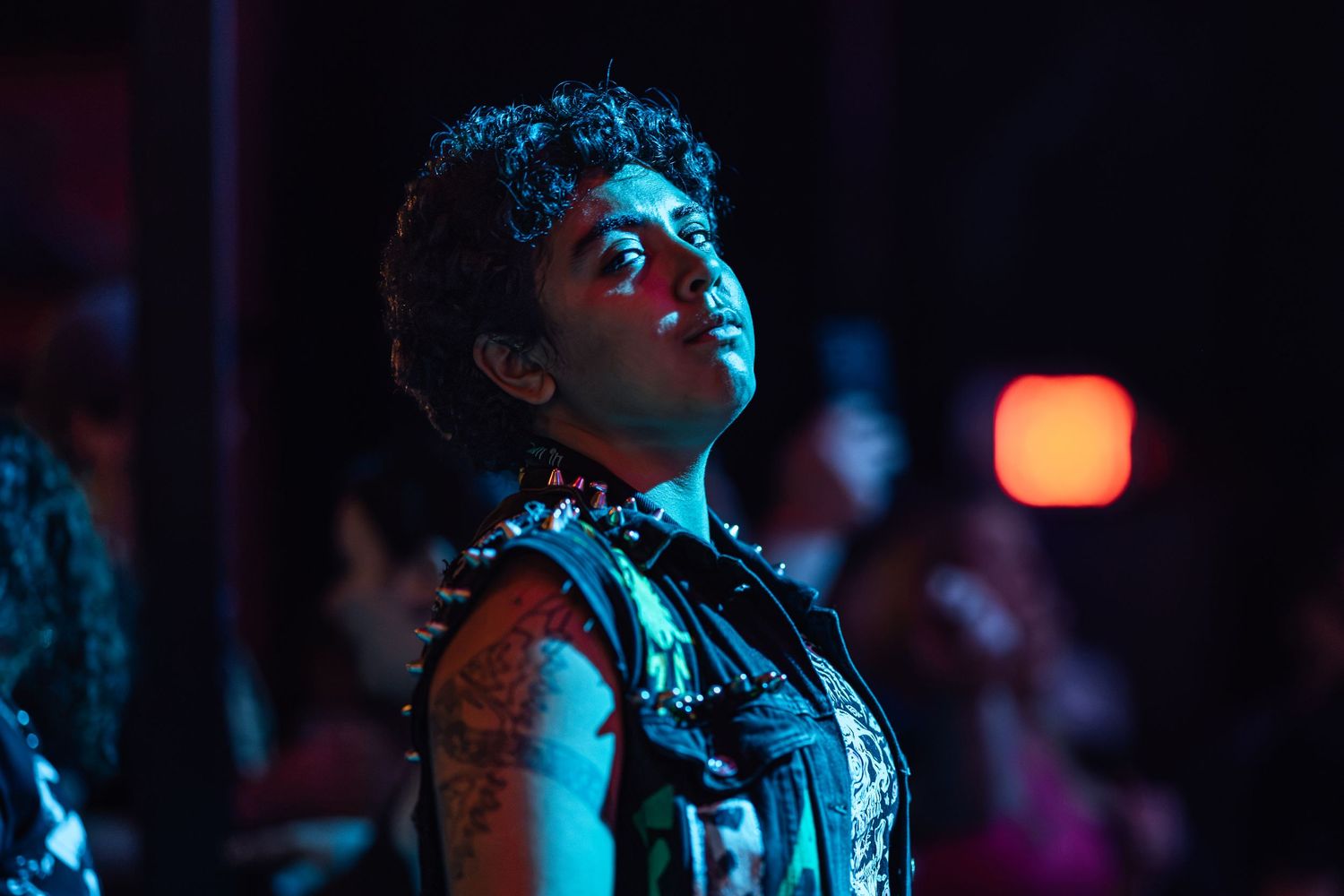 A tattooed person in punk attire gazes upward under dramatic blue and red nightclub lighting.