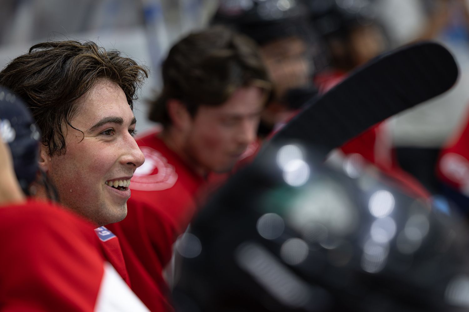 Smiling young hockey player in red jersey sitting on the bench with teammates during a game.