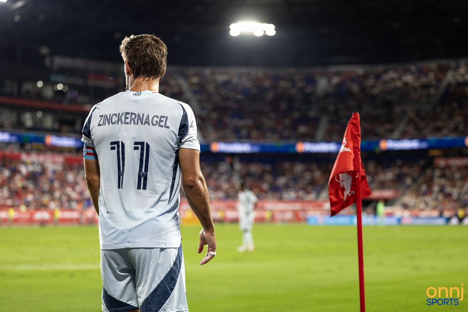 Soccer player Zinckernagel wearing jersey number 11 stands near a red corner flag during a stadium match.