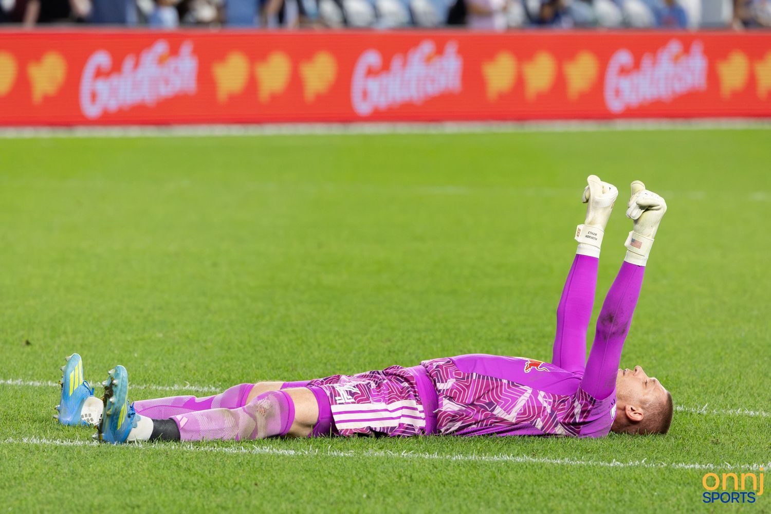 Soccer goalkeeper in purple kit lying on grass field after making a save during a match.