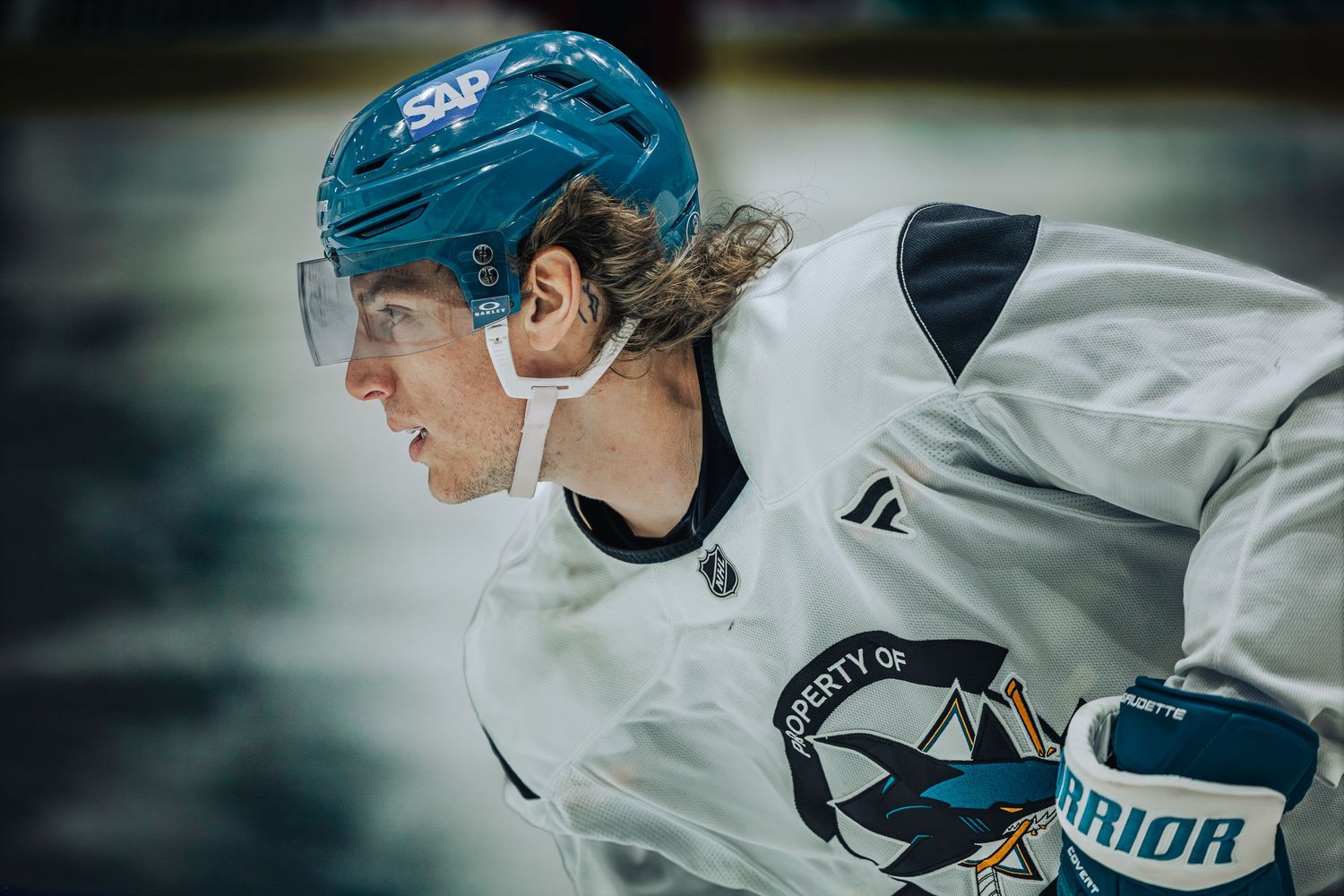 San Jose Sharks hockey player wearing teal helmet and white jersey leaning forward on ice during game.