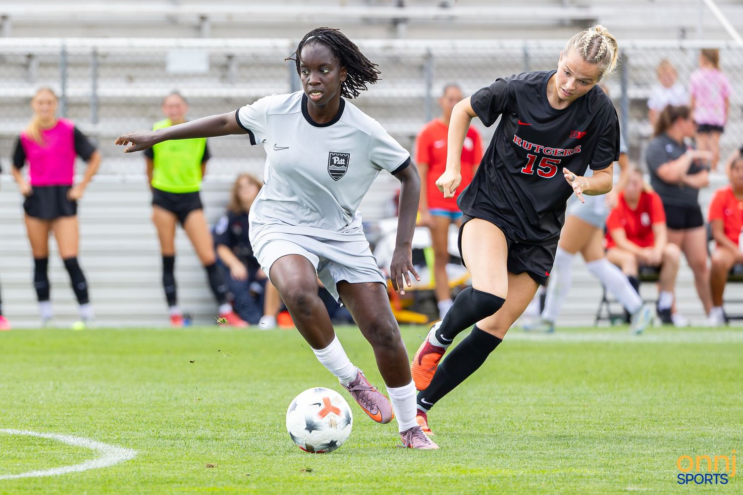 Two female soccer players compete for the ball during a match, one in white and one in black uniform.