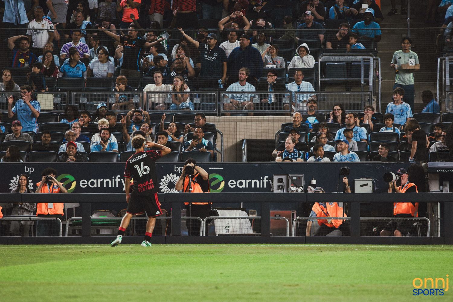 Soccer player wearing jersey number 16 celebrates on the field during an MLS match with fans in the stadium background.