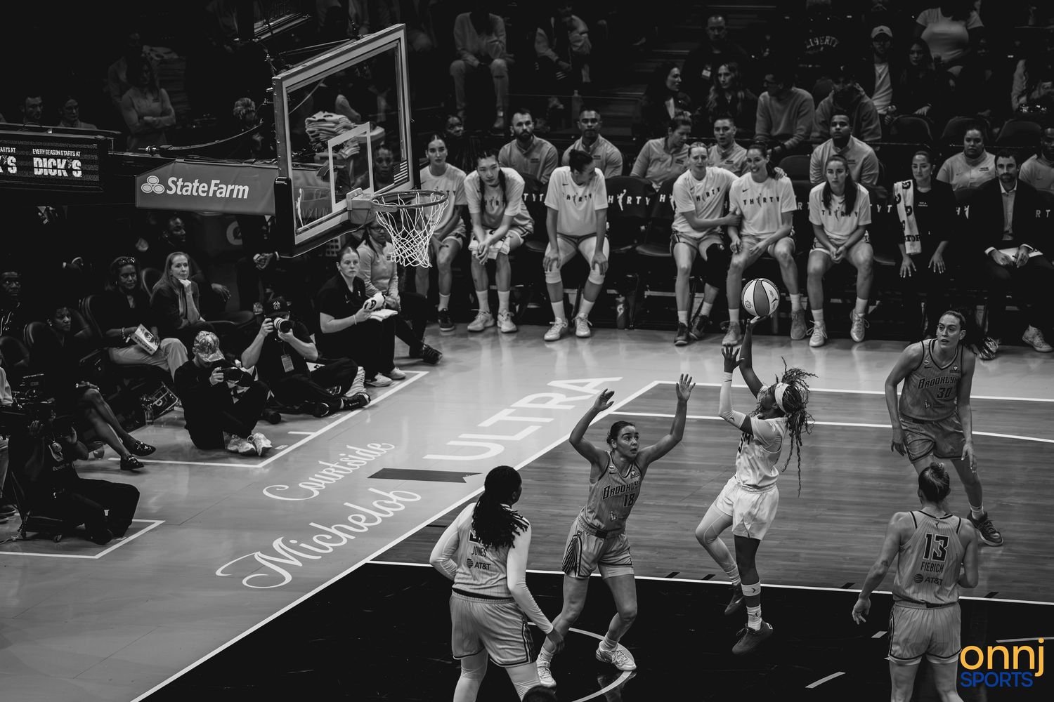 Black and white photo of a WNBA basketball game with players competing near the basket in a packed arena.