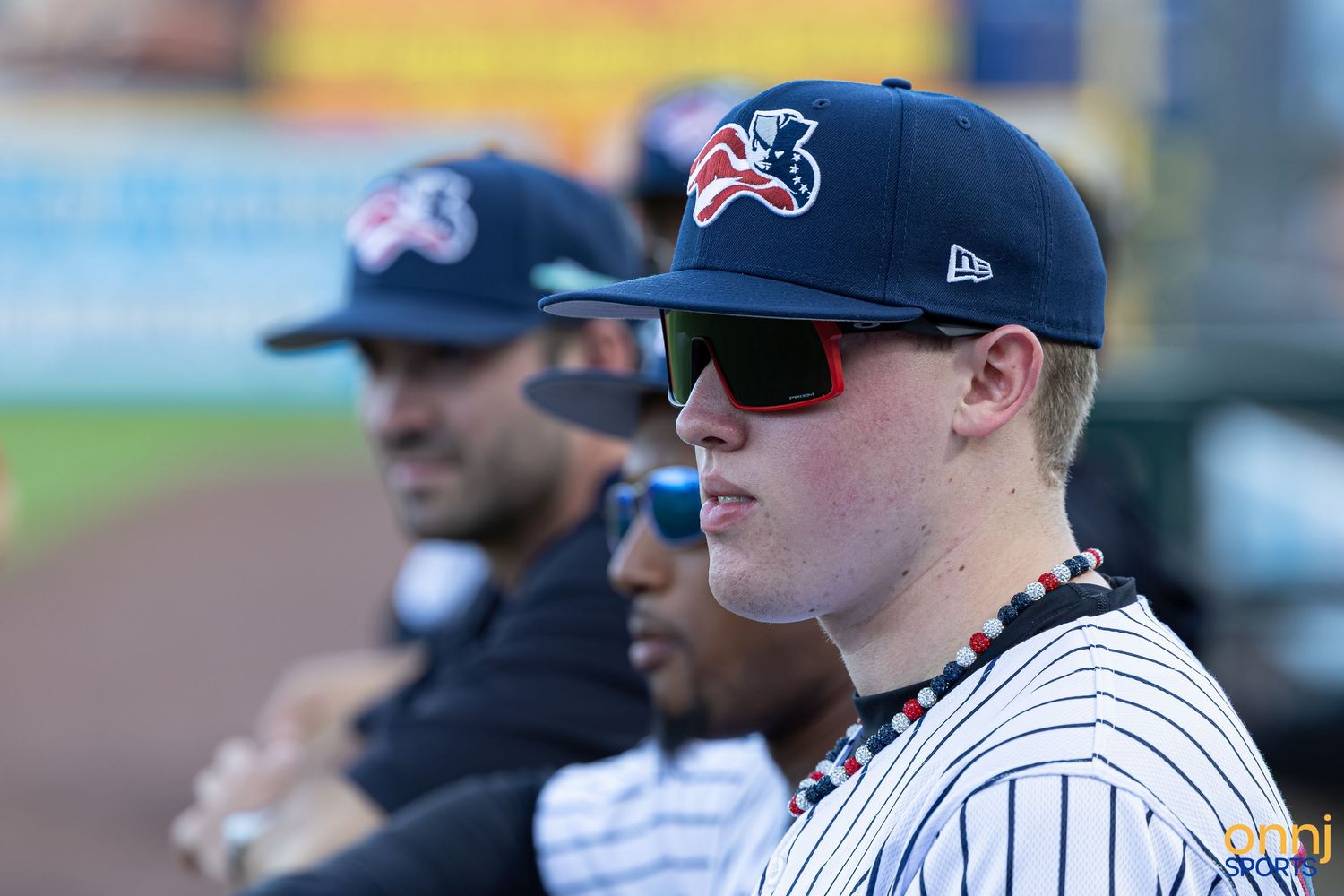 Baseball players in pinstripe uniforms and navy caps stand in the dugout during a game.