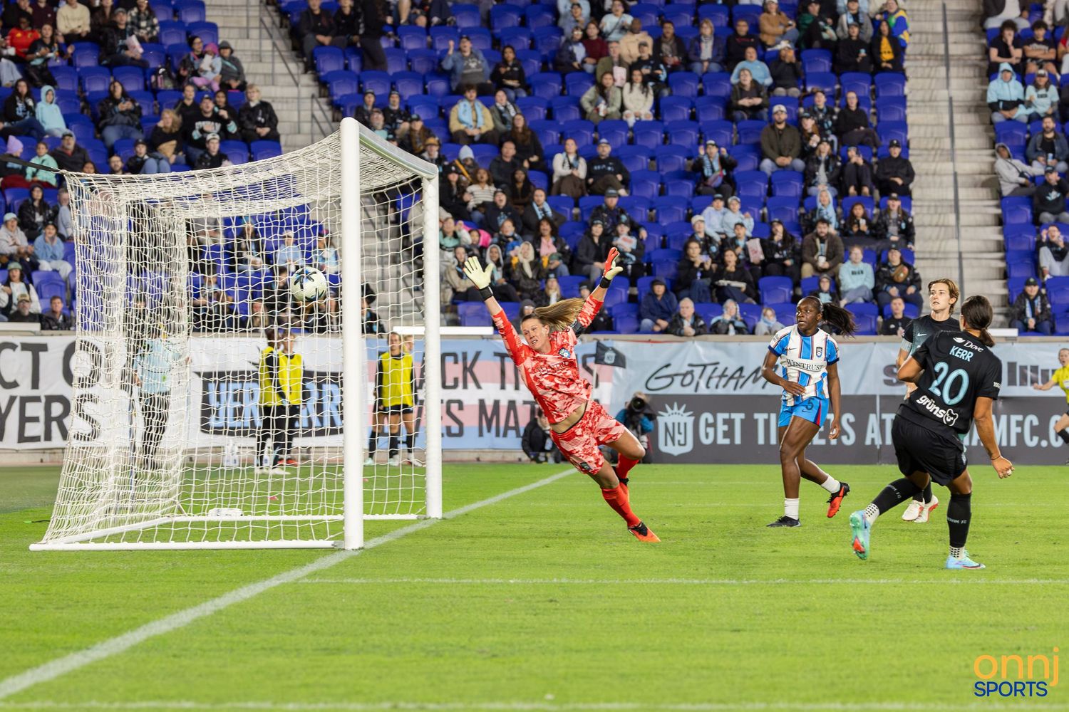 Soccer player number 20 attempts a shot on goal as goalkeeper dives to make a save during a night match.