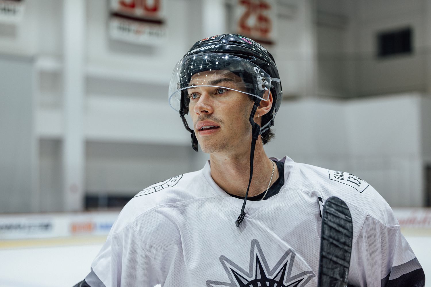 Young male ice hockey player in white jersey and helmet standing on rink, looking focused during practice.