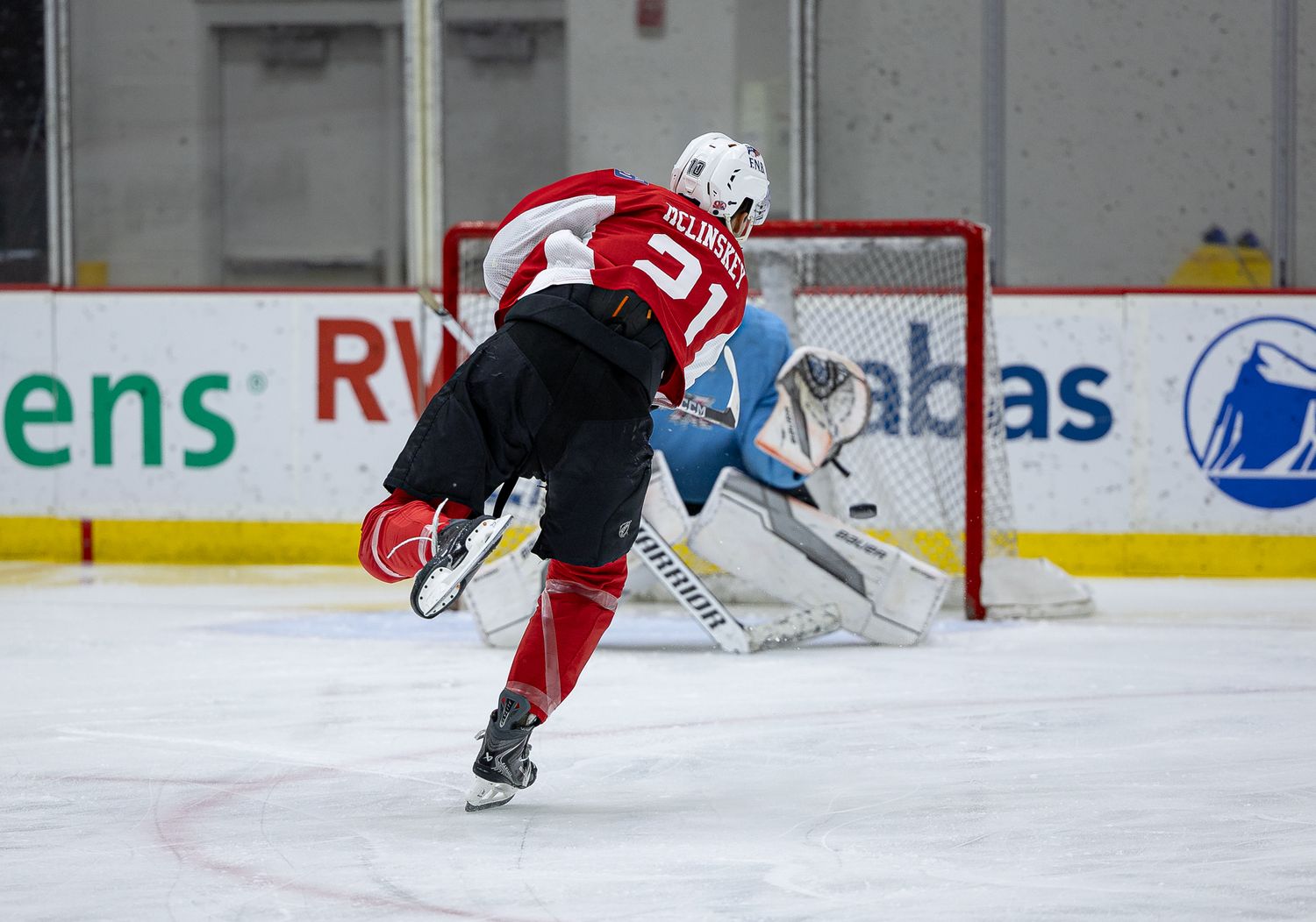 Hockey player #31 in red uniform takes a shot on goal during an NHL practice session on indoor ice rink.