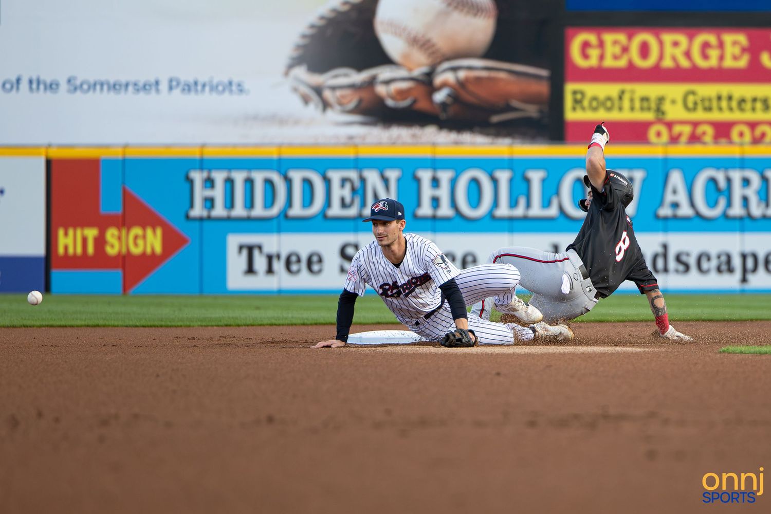 Baseball player slides into second base as infielder attempts tag during Somerset Patriots minor league game.