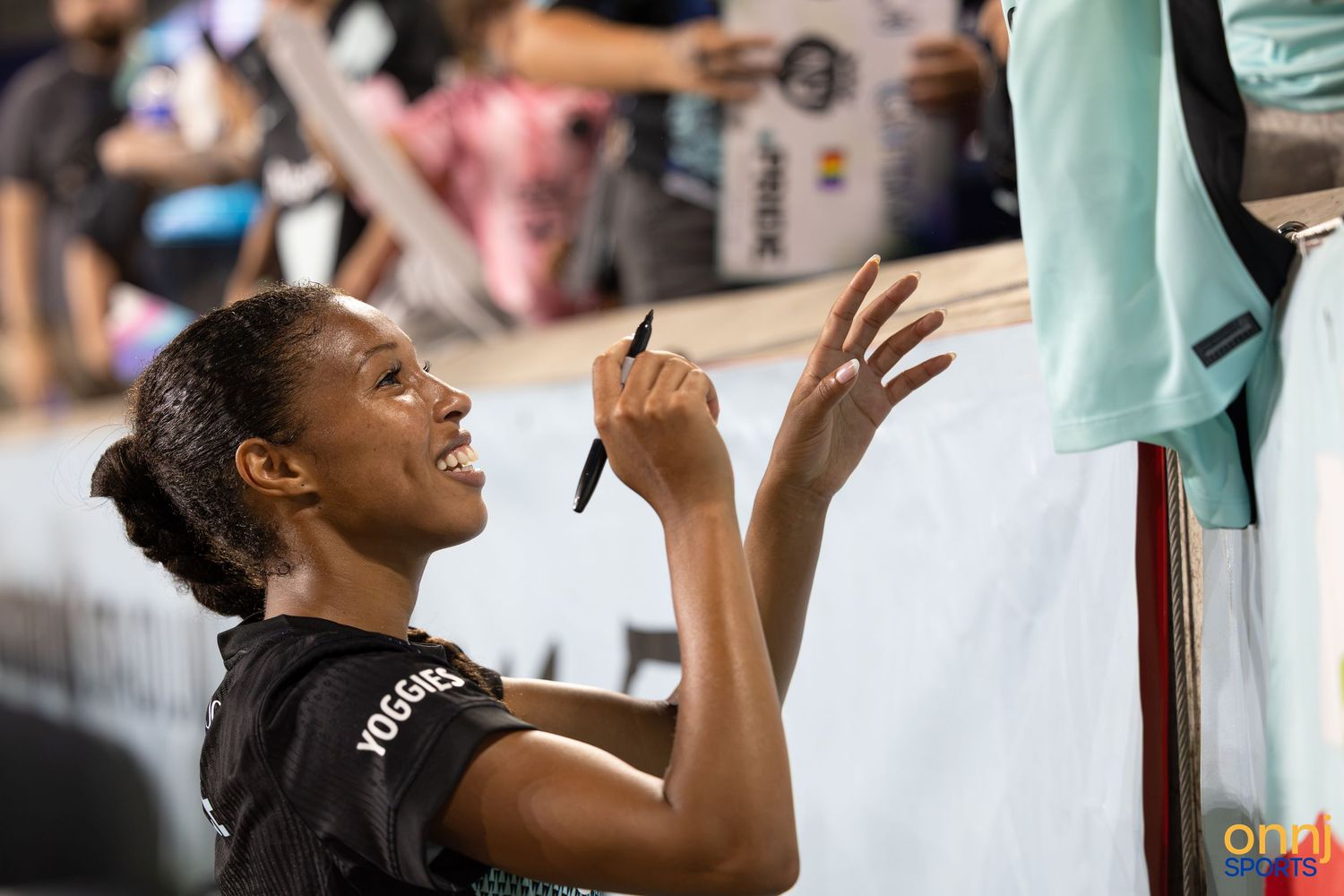Athlete smiling while signing autographs for fans at a sporting event.
