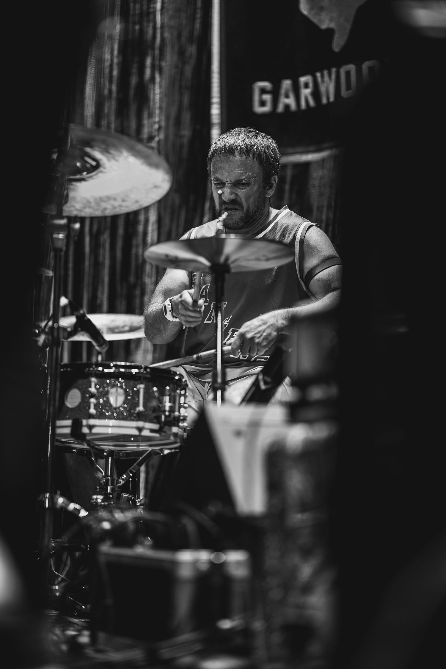 Black and white photo of an intense male drummer performing on stage at Garwood venue.
