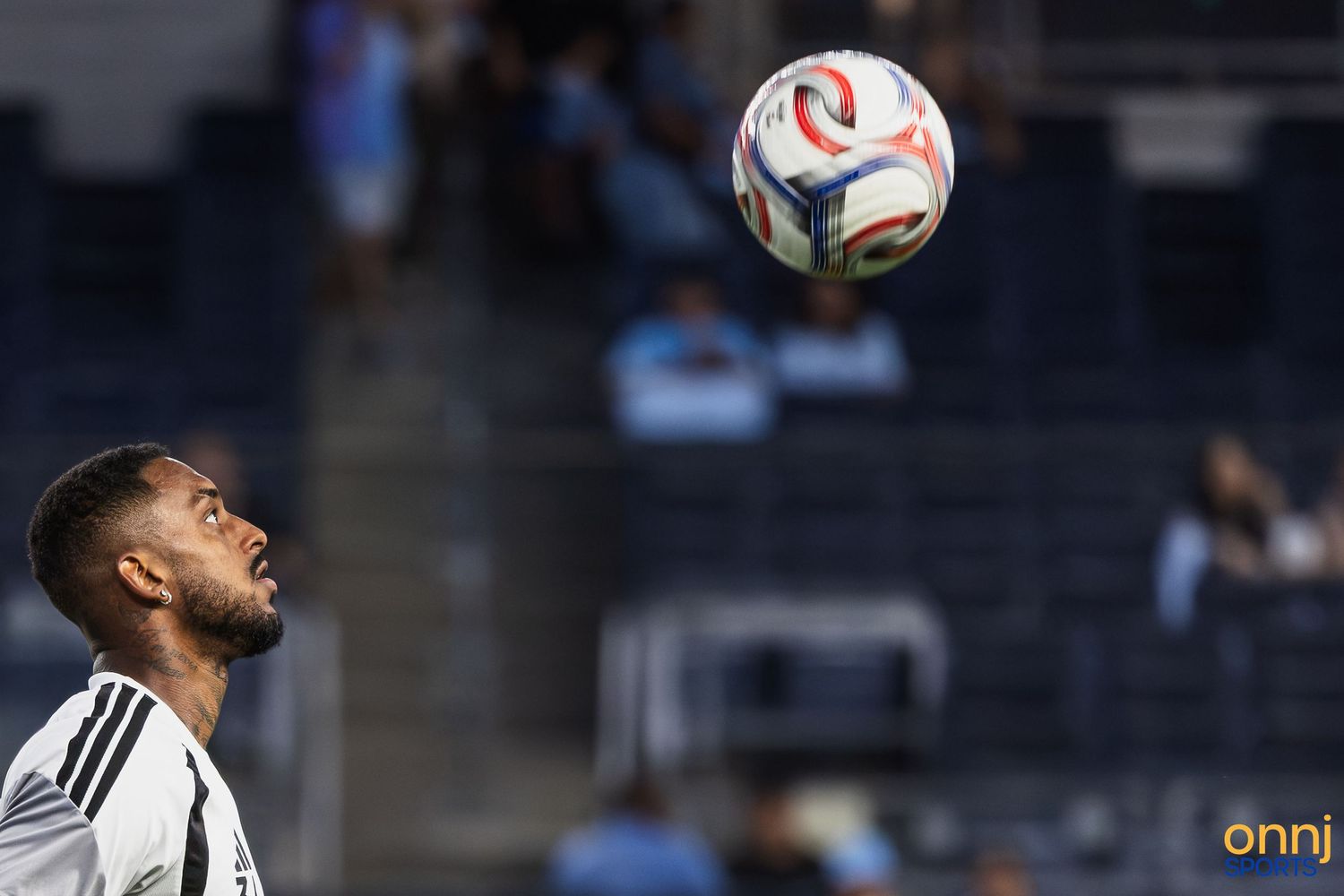 Soccer player in white jersey heading a ball during an MLS match on a sunny day.