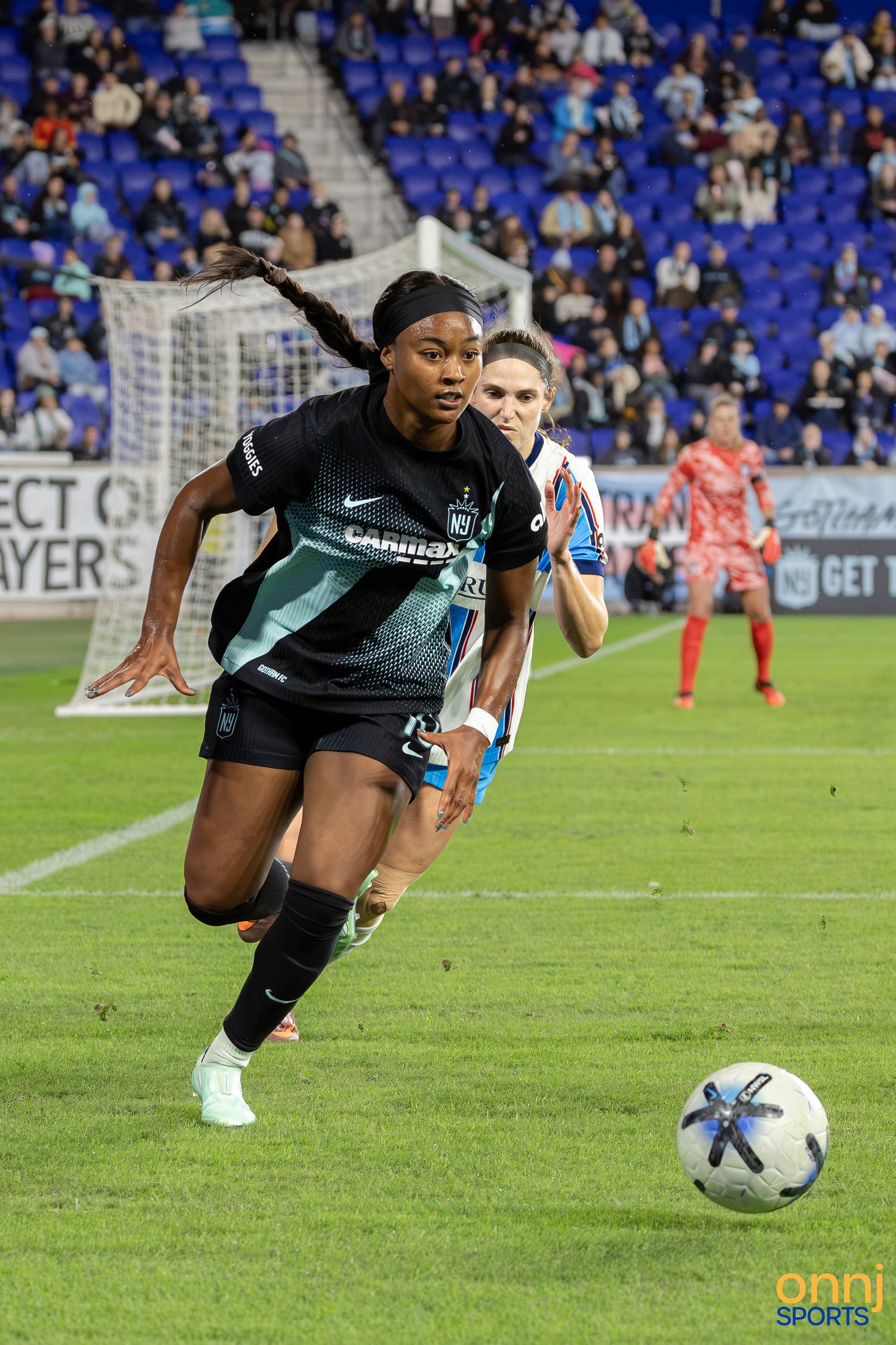 Female soccer player in black uniform chasing the ball during a professional women's soccer match under stadium lights.
