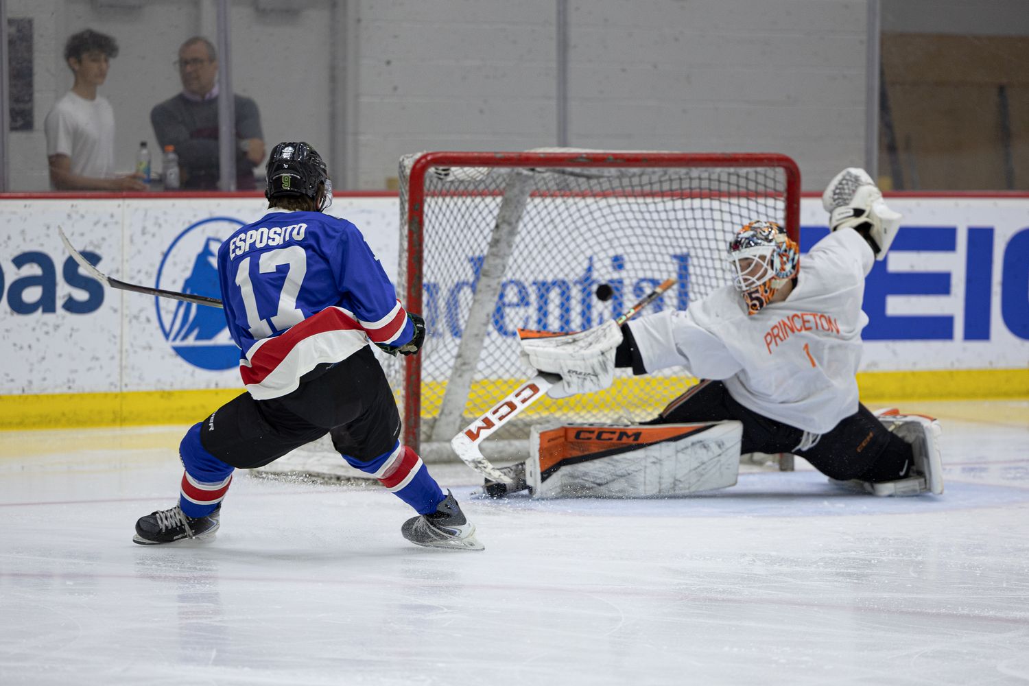 Hockey player #17 Grosso takes a shot on goal against a goalie in an indoor ice rink during a competitive game.