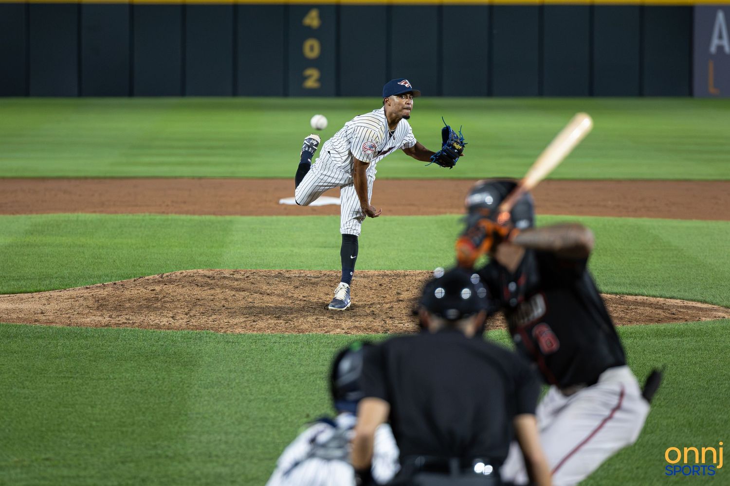 Baseball pitcher mid-throw on mound as batter and catcher await the pitch during a professional night game.
