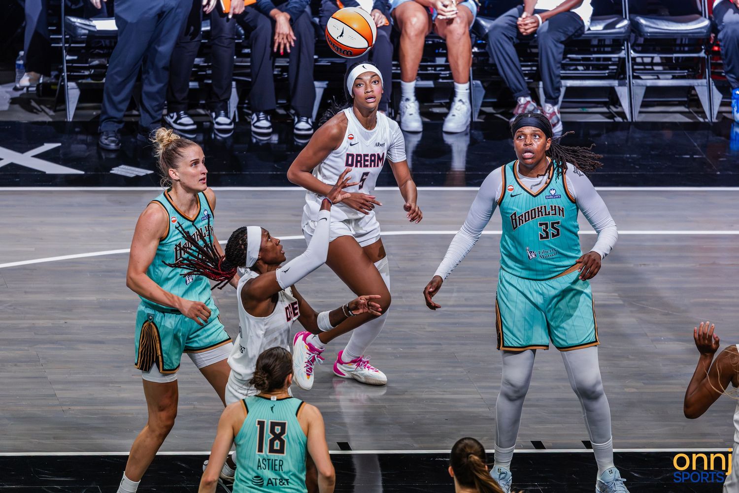 WNBA players compete in an intense basketball game, with one player leaping to pass the ball during a match.