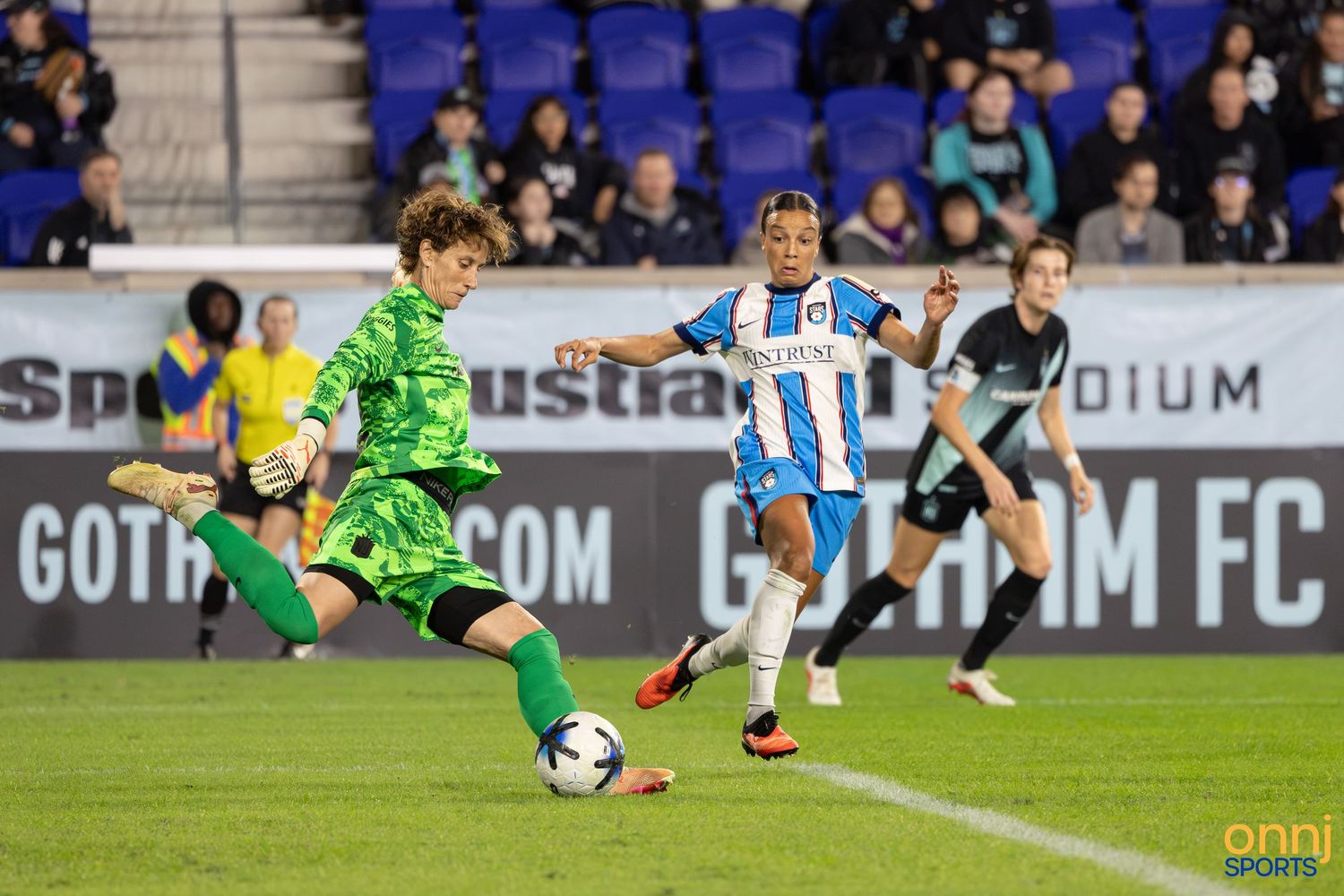 Soccer players compete for the ball during a Gotham FC match, with a goalkeeper in green kit making a clearance.