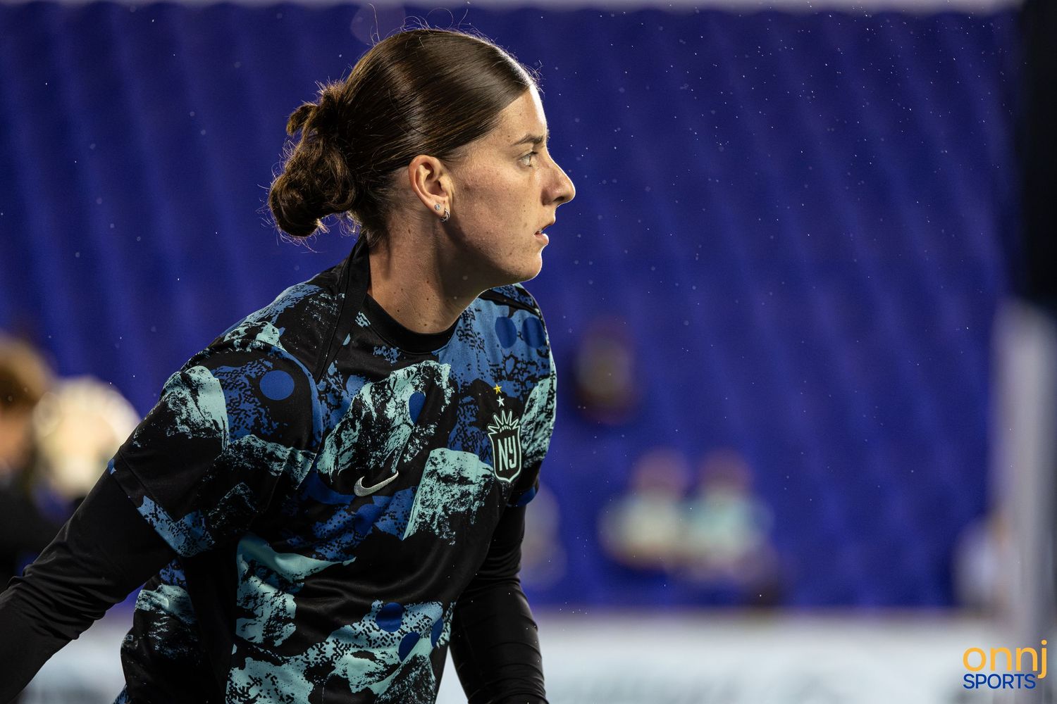 Female athlete in blue camo athletic wear focuses intently during an indoor sports warm-up session.