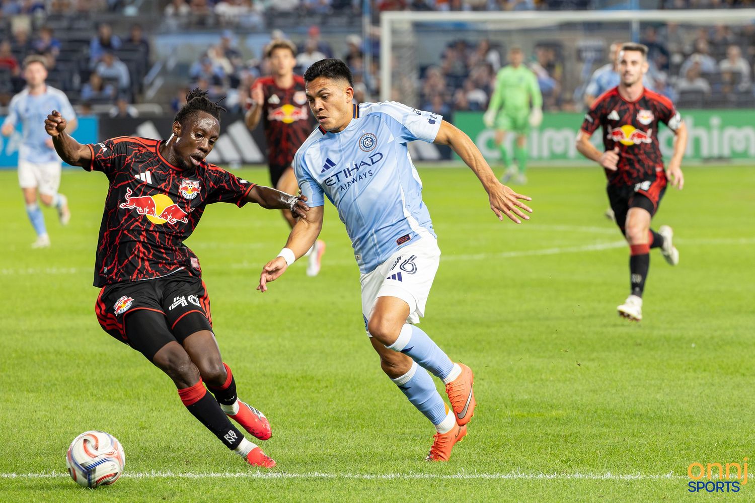Two MLS soccer players compete for the ball during a NYCFC vs New York Red Bulls match at Yankee Stadium.