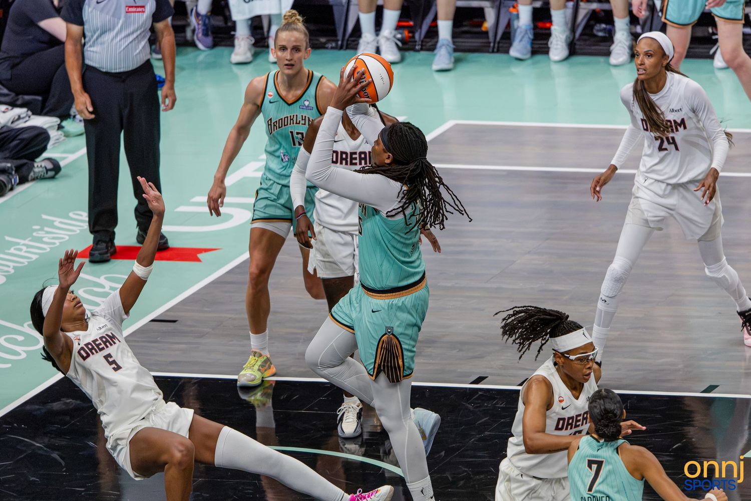 WNBA players compete in an intense basketball game, with one player shooting while others defend on the court.