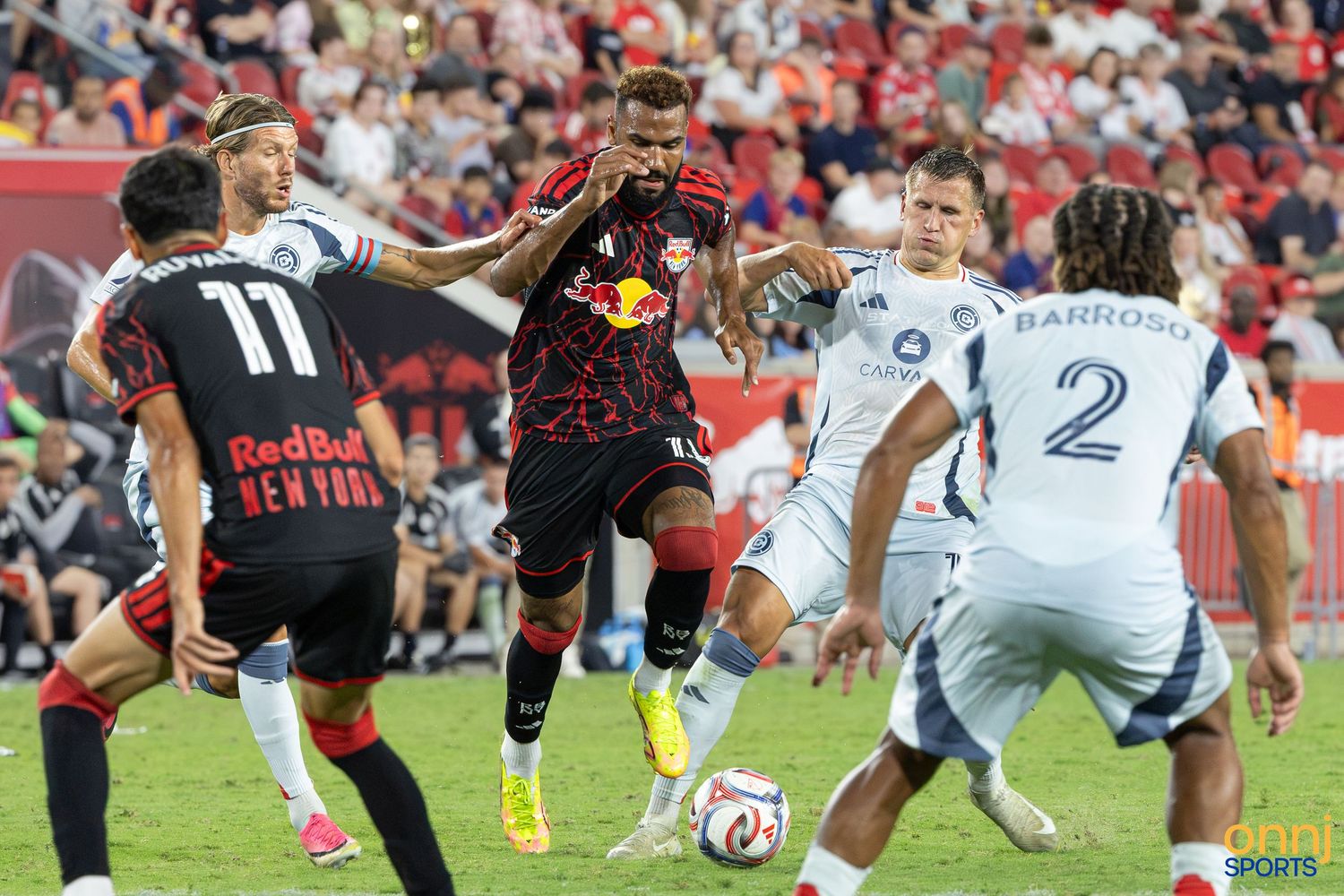 New York Red Bulls player dribbles past opponents in an MLS soccer match under bright stadium lights.