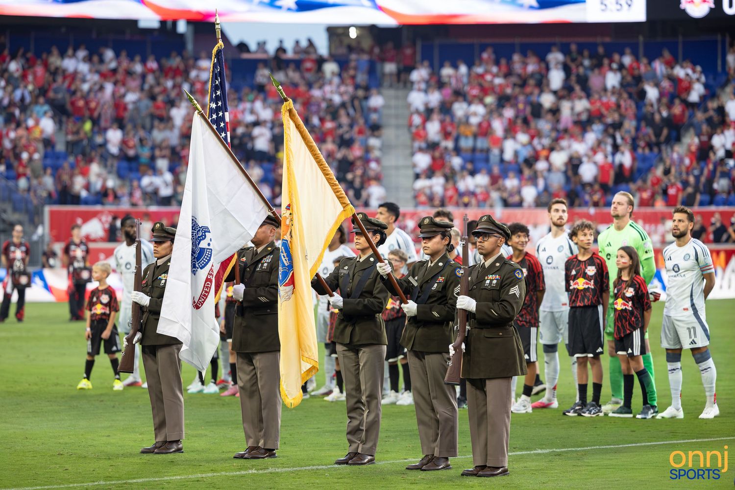 Military honor guard presents flags at an MLS soccer match ceremony with players lined up on the field.