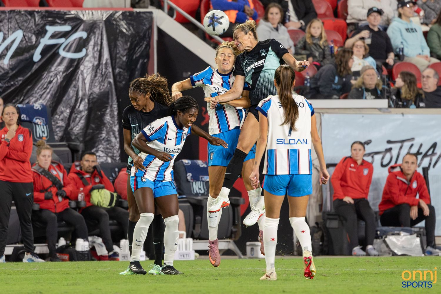 Women's soccer players compete for a header during an intense NWSL match under stadium lights.