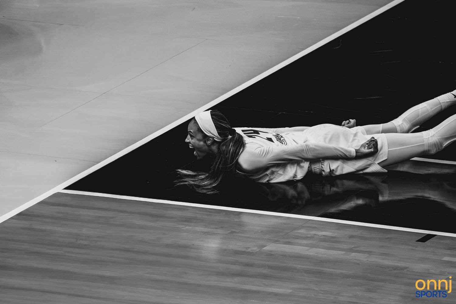 Black and white photo of a basketball player lying on the court floor during a game.