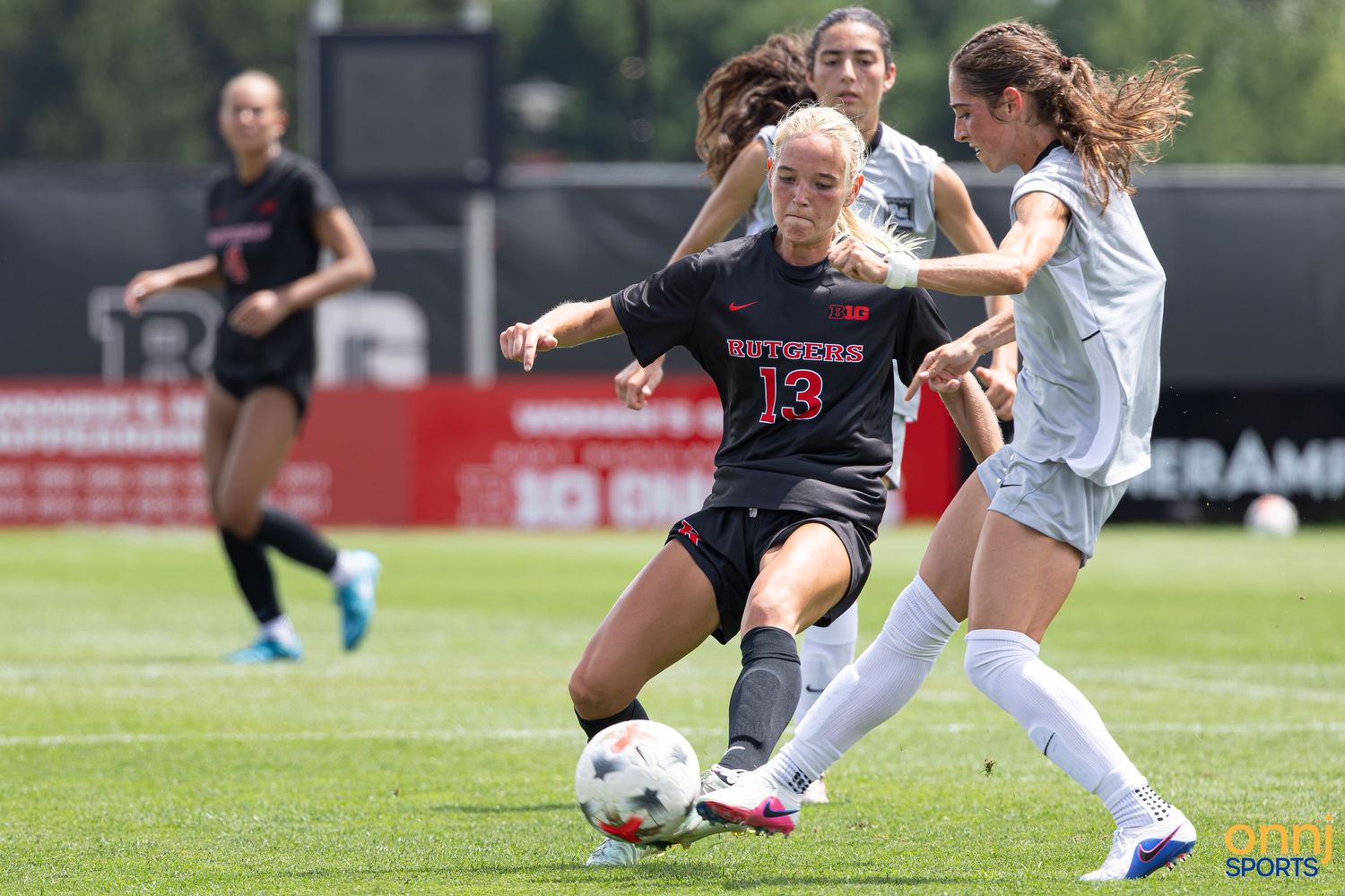 Rutgers soccer player #13 battles opponent for ball during competitive women's college soccer match on green field.