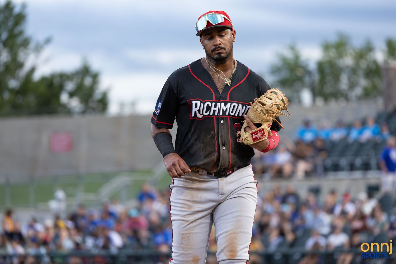 Richmond baseball player in dark uniform with red accents jogs on field holding brown glove during outdoor game.