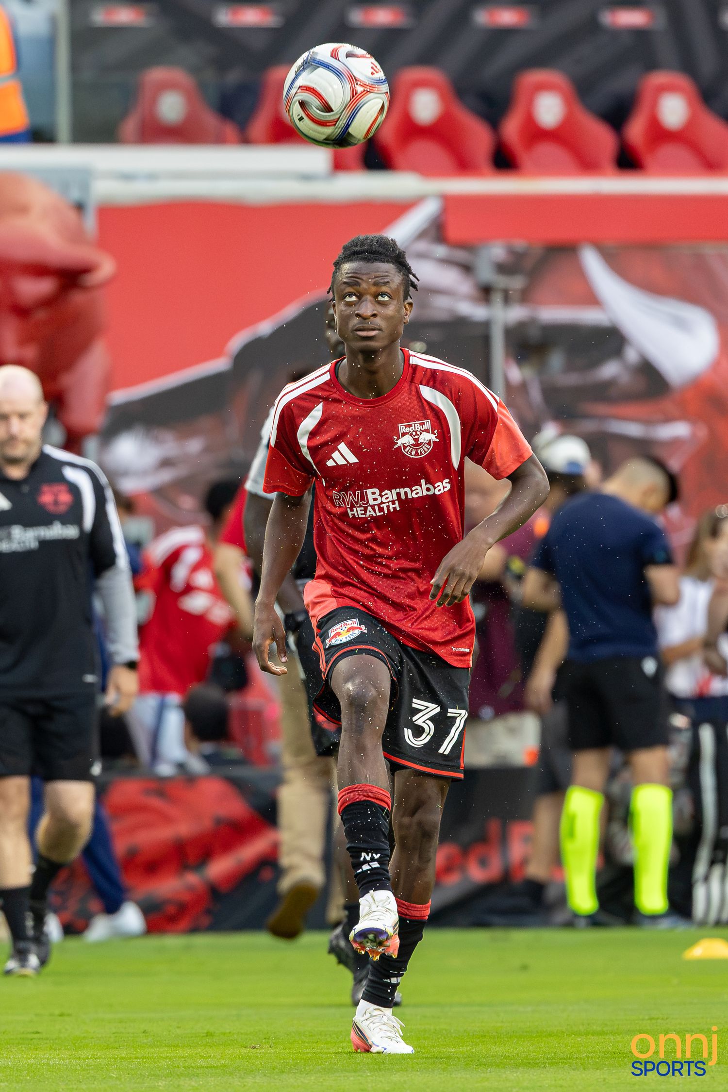 New York Red Bulls player #31 in red jersey heads soccer ball during MLS match at Red Bull Arena.